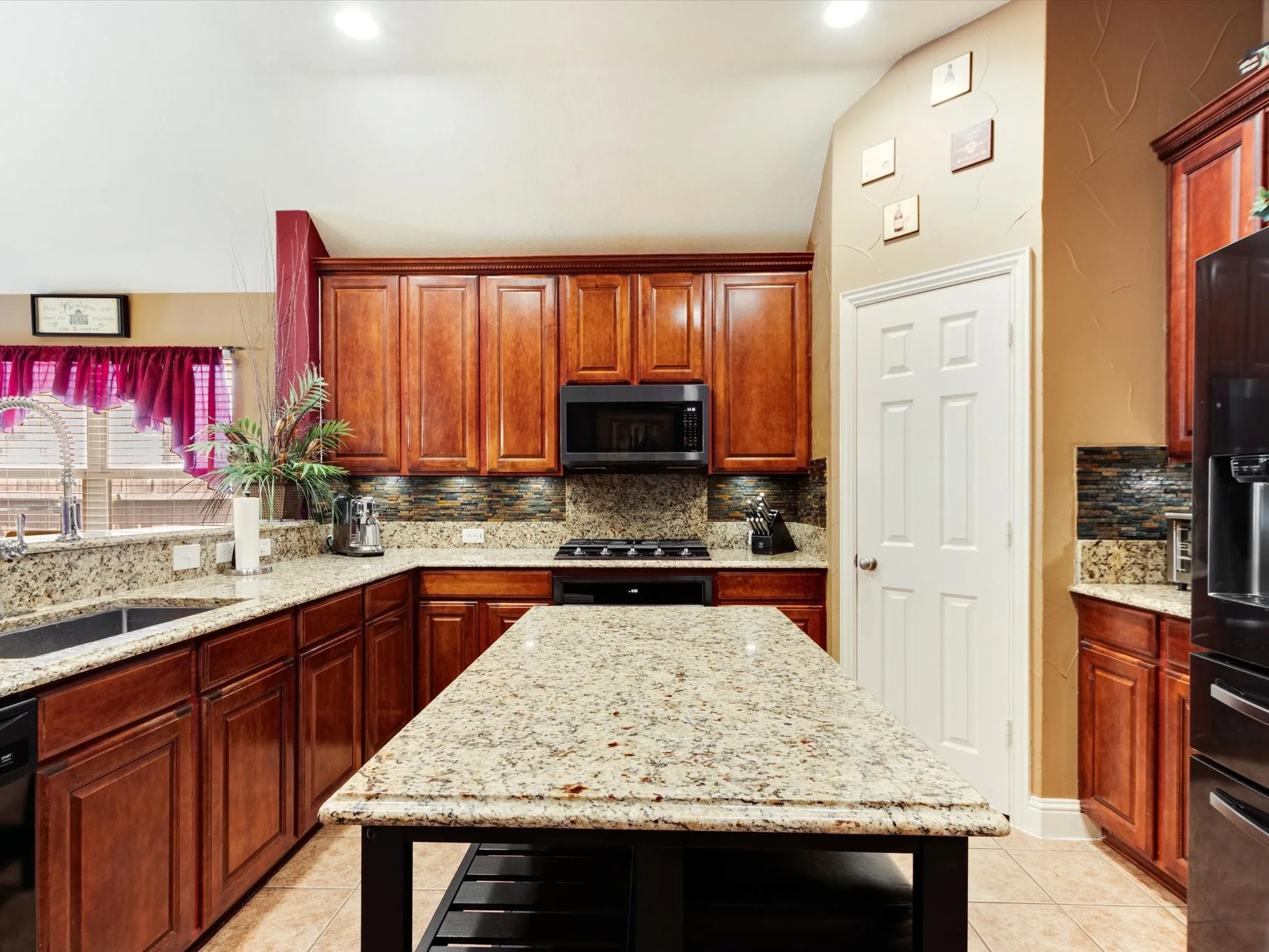 Kitchen featuring an island, granite countertops, wood cabinetry, built-in microwave, and tile flooring