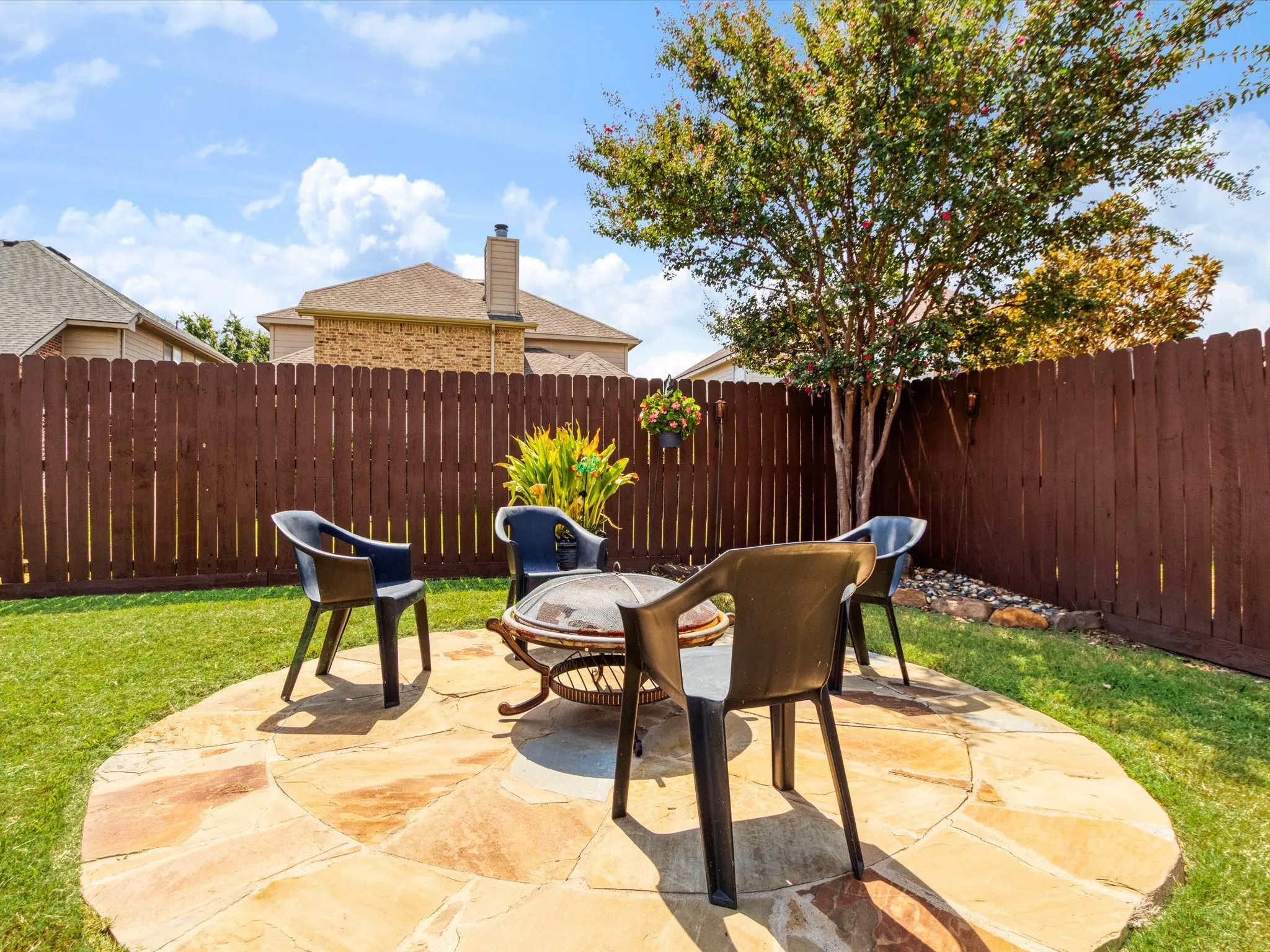 Expansive backyard featuring a natural stone patio, manicured lawn, mature tree, and privacy fencing