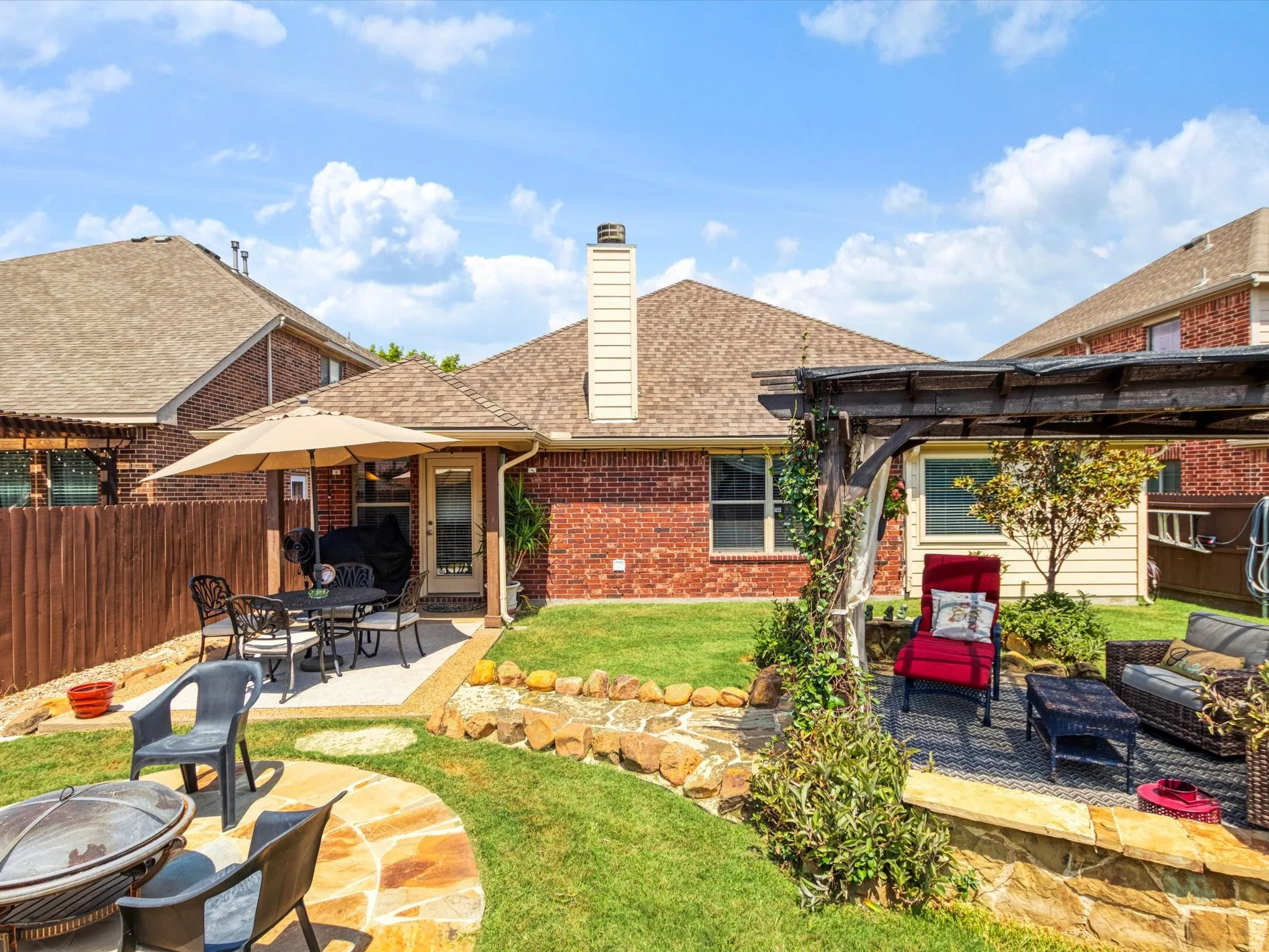 Expansive backyard featuring a manicured lawn, flagstone patio, brick exterior, and a wooden pergola