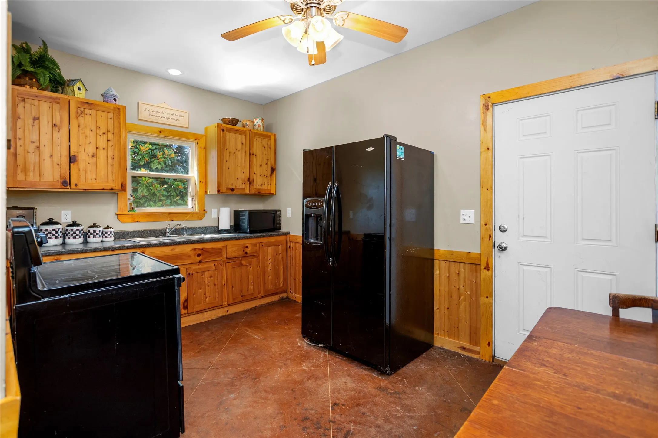 Guest quarter kitchen with dark countertops, black appliances, wainscoting, ceiling fan, and wood cabinets