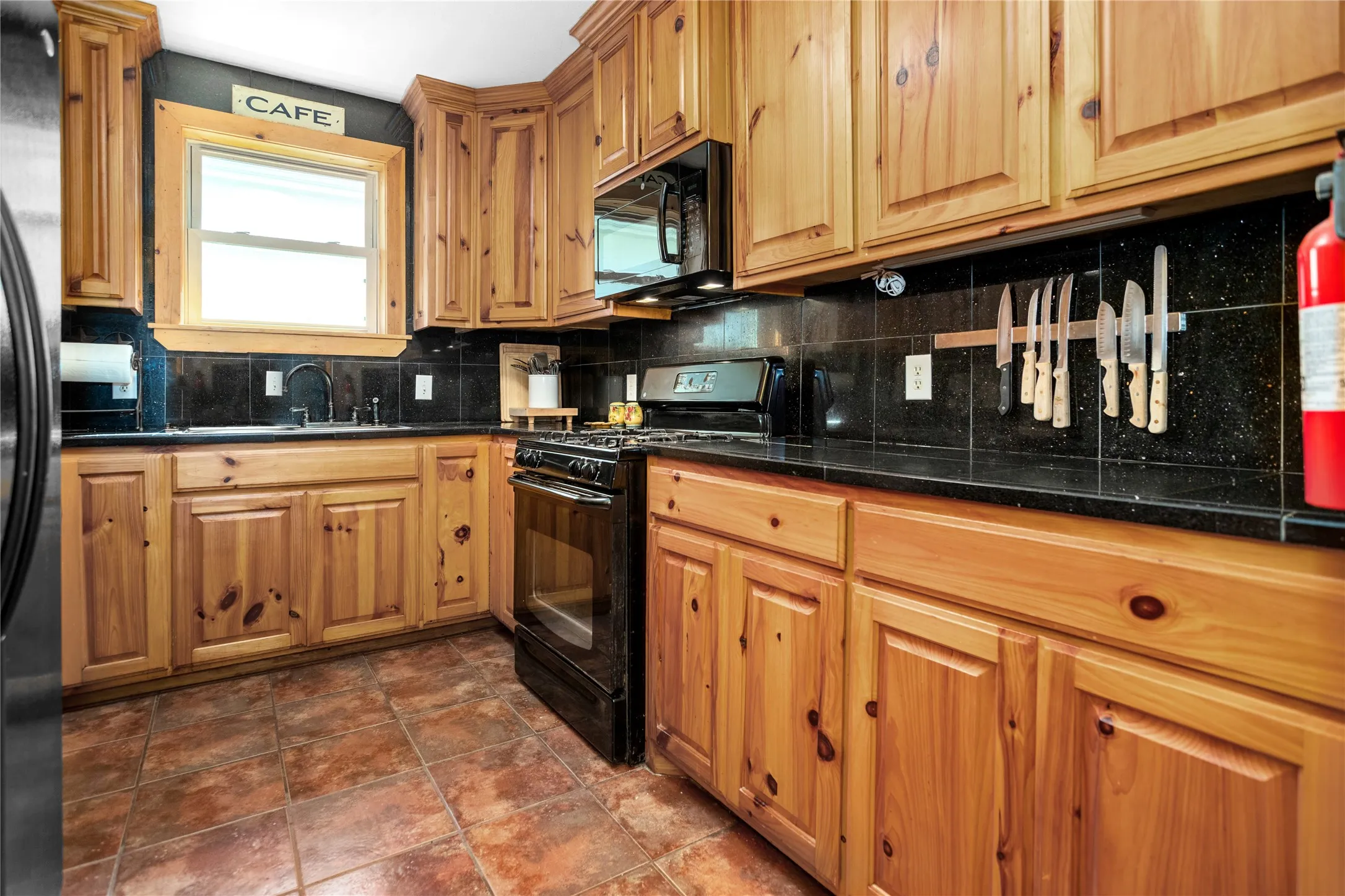 Kitchen featuring black appliances, decorative backsplash, wood cabinetry, and tile floors