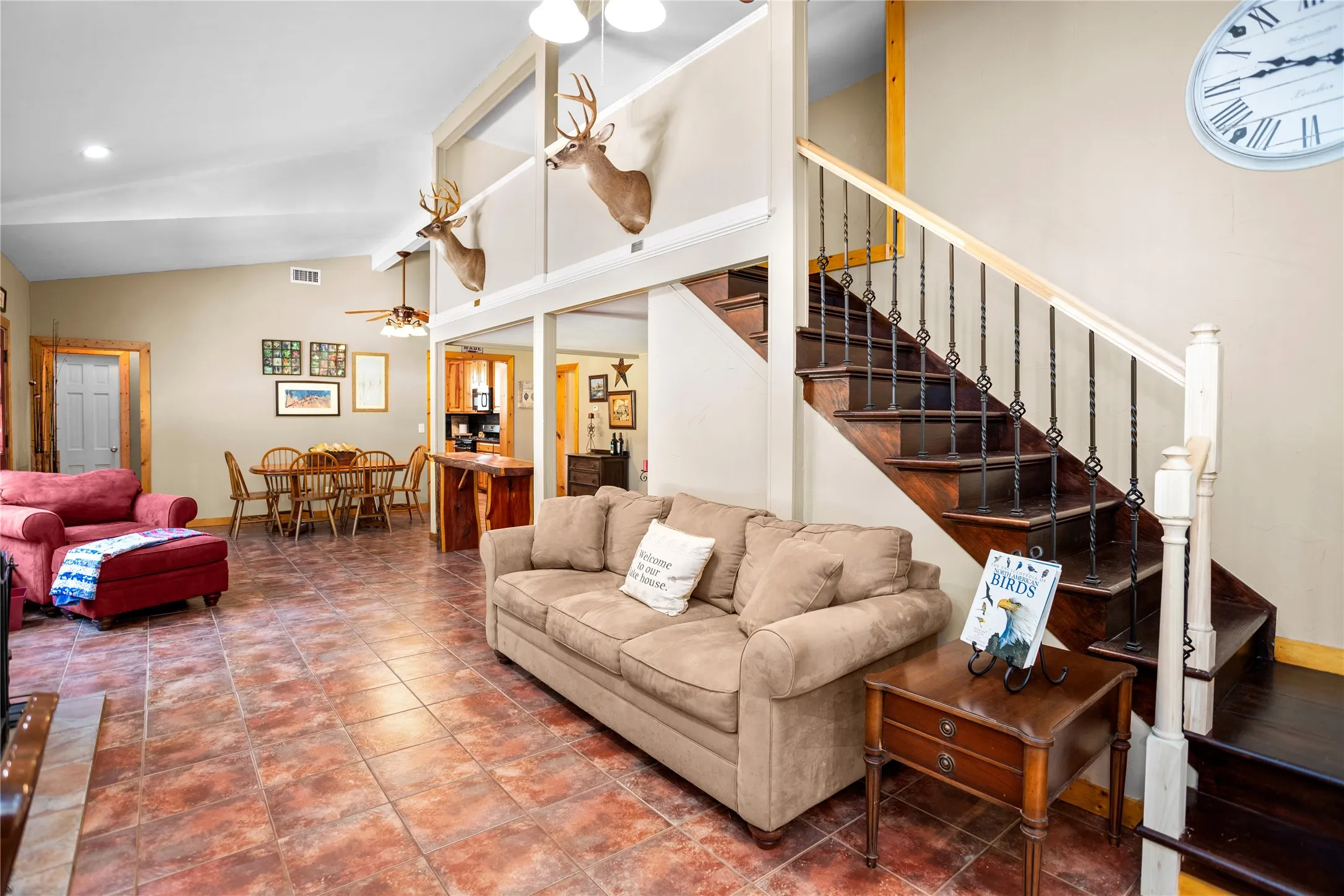 Living area featuring stairway, vaulted ceiling, a ceiling fan, and tile flooring