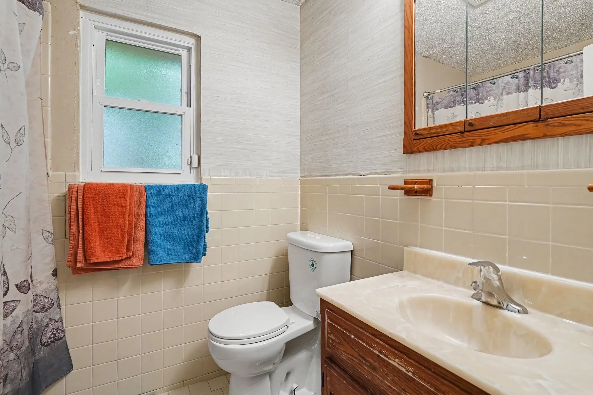 White toilet with a built-in cistern, a single-pane window with frosted glass, and a wood-finish vanity with an integrated sink