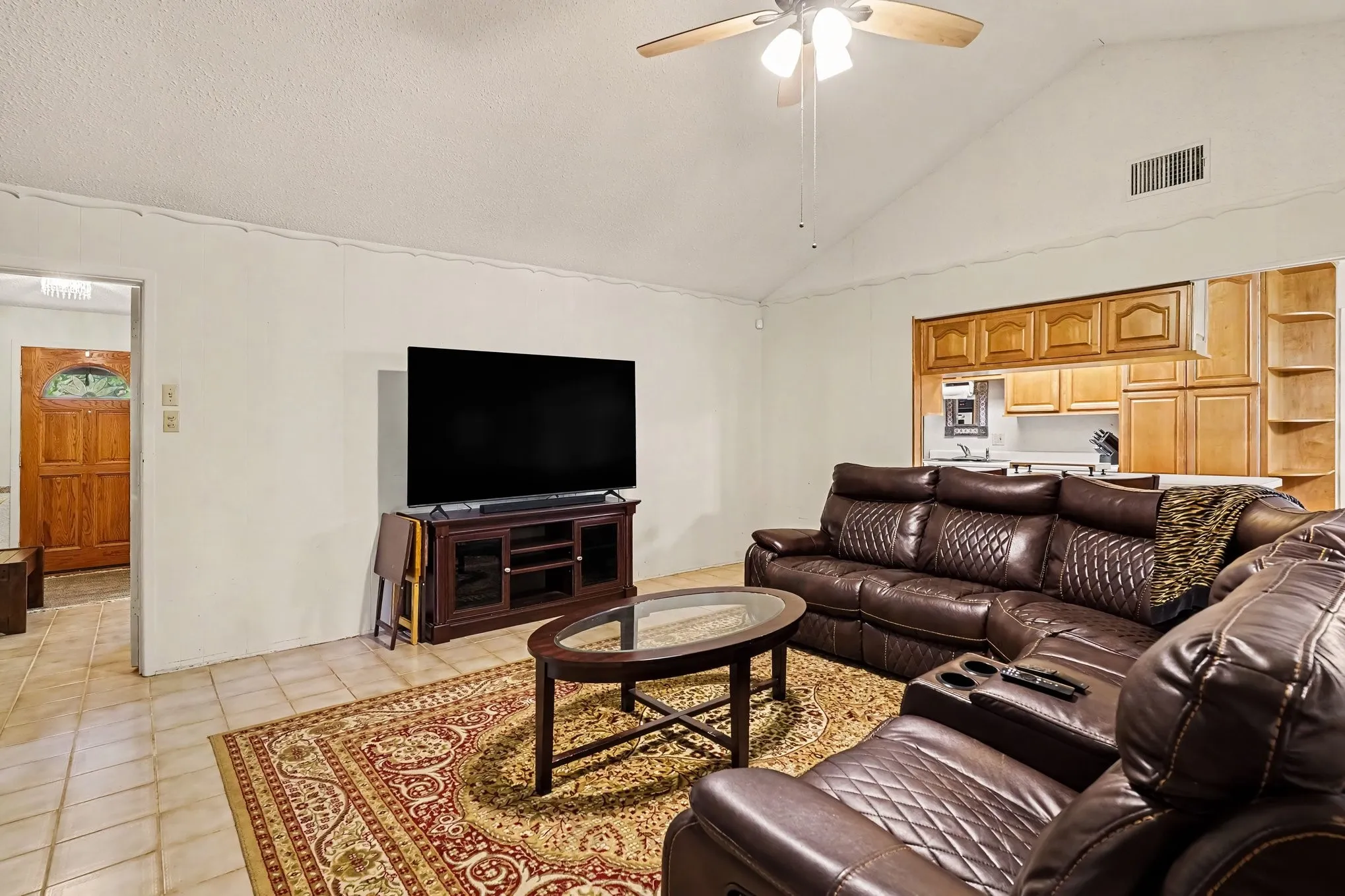 Vaulted ceiling, ceiling fan, wood-finish cabinetry, tile flooring, wood entry door with glass insert