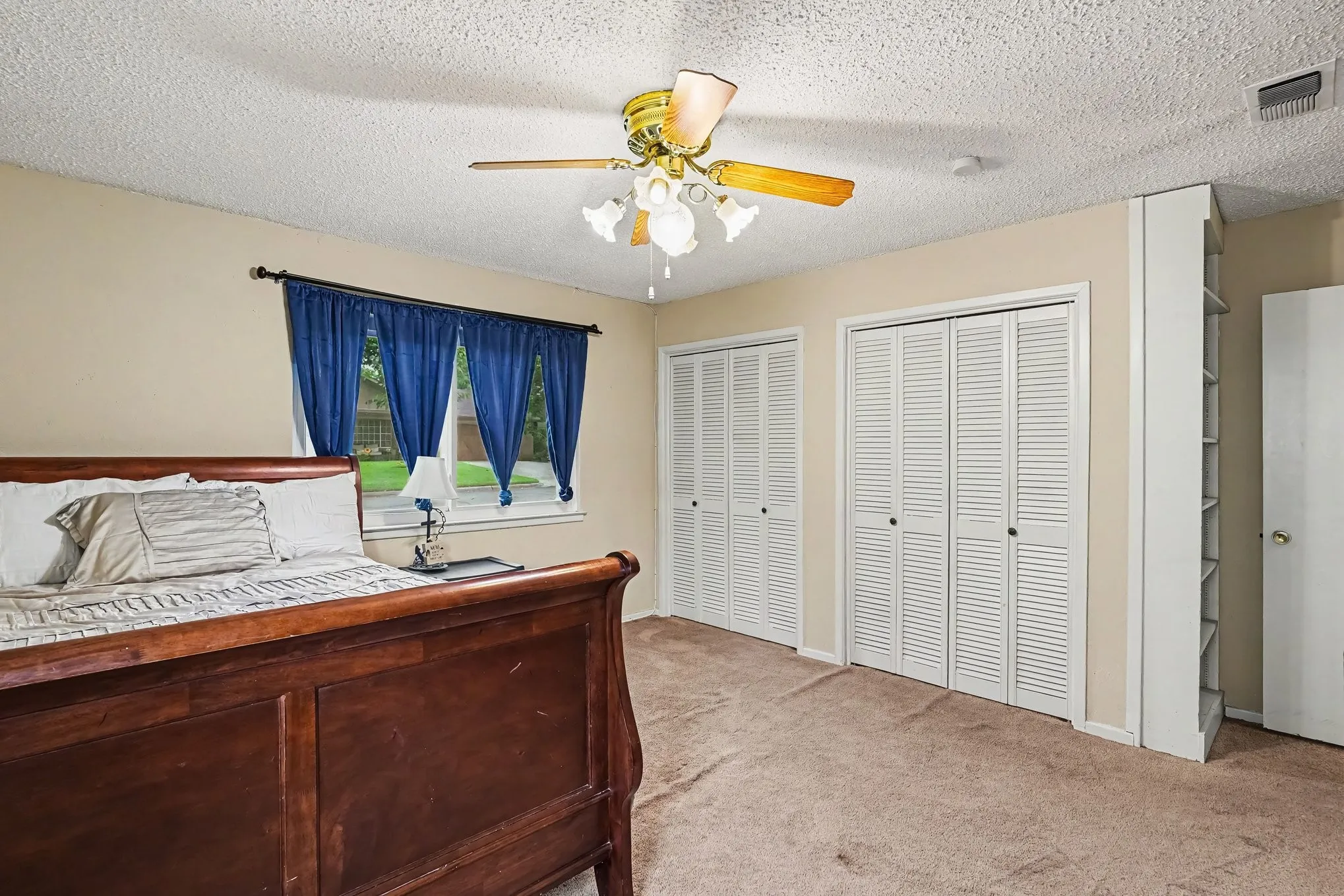 Dual bi-fold louvered closet doors, built-in shelving, carpet flooring, and a ceiling fan with integrated lighting