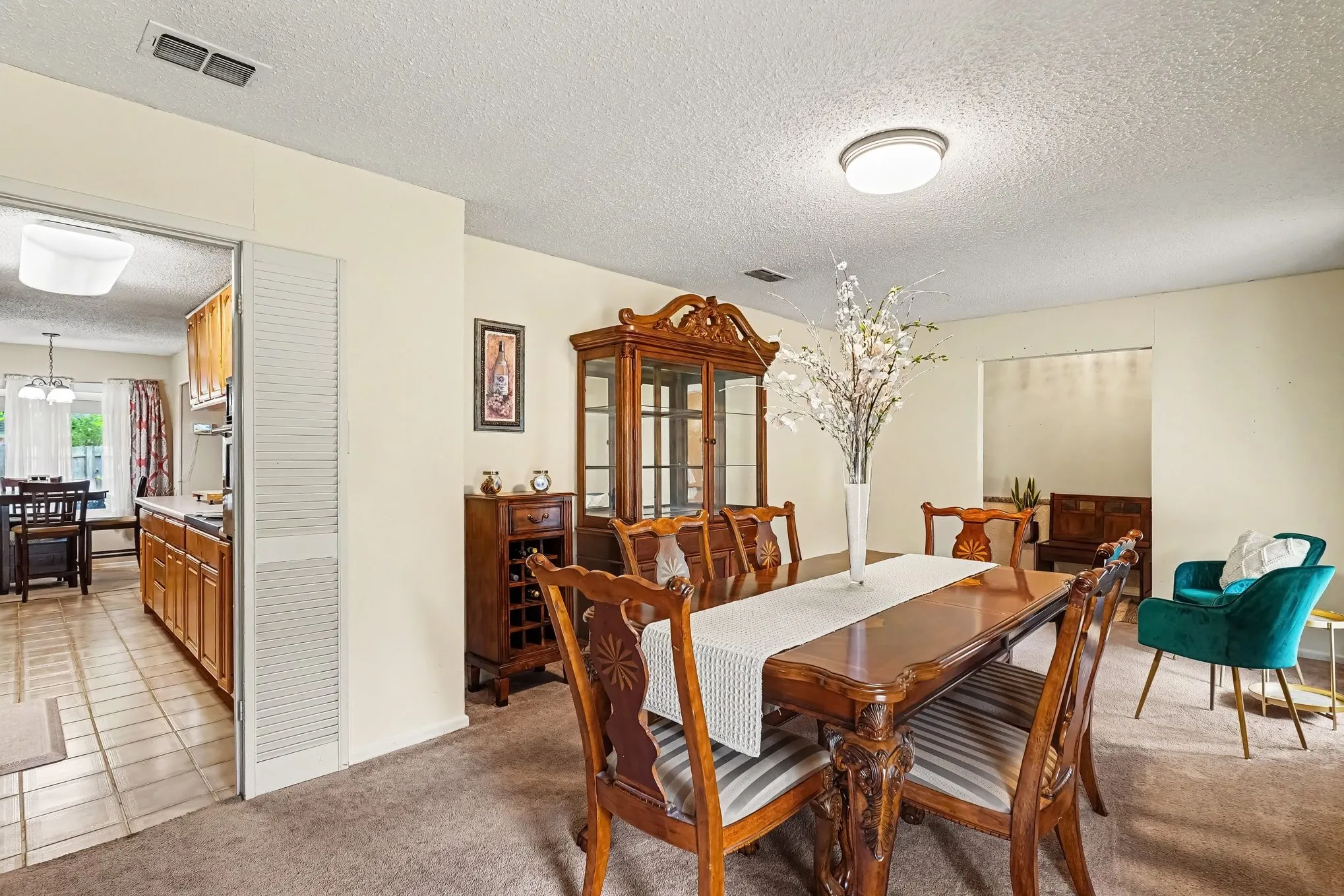 Carpeted dining area with a flush-mount light fixture, featuring an open doorway to an additional room