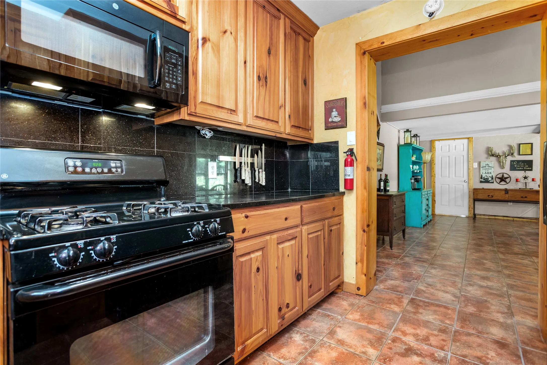 Kitchen with black appliances, tasteful backsplash, dark stone counters, tile floors, and wood cabinetry