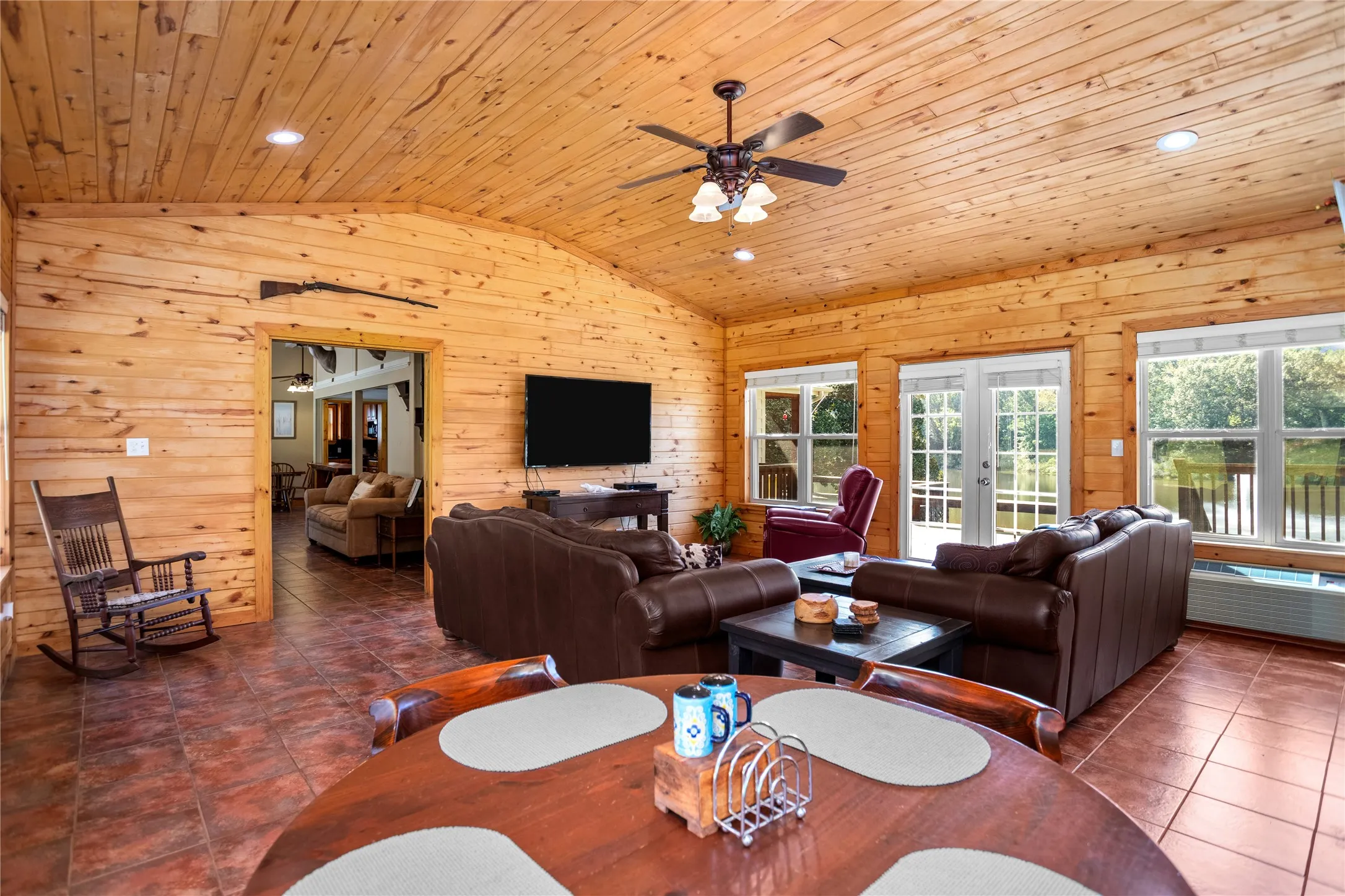 Living room featuring lofted ceiling, french doors, wood walls, recessed lighting, and ceiling fan