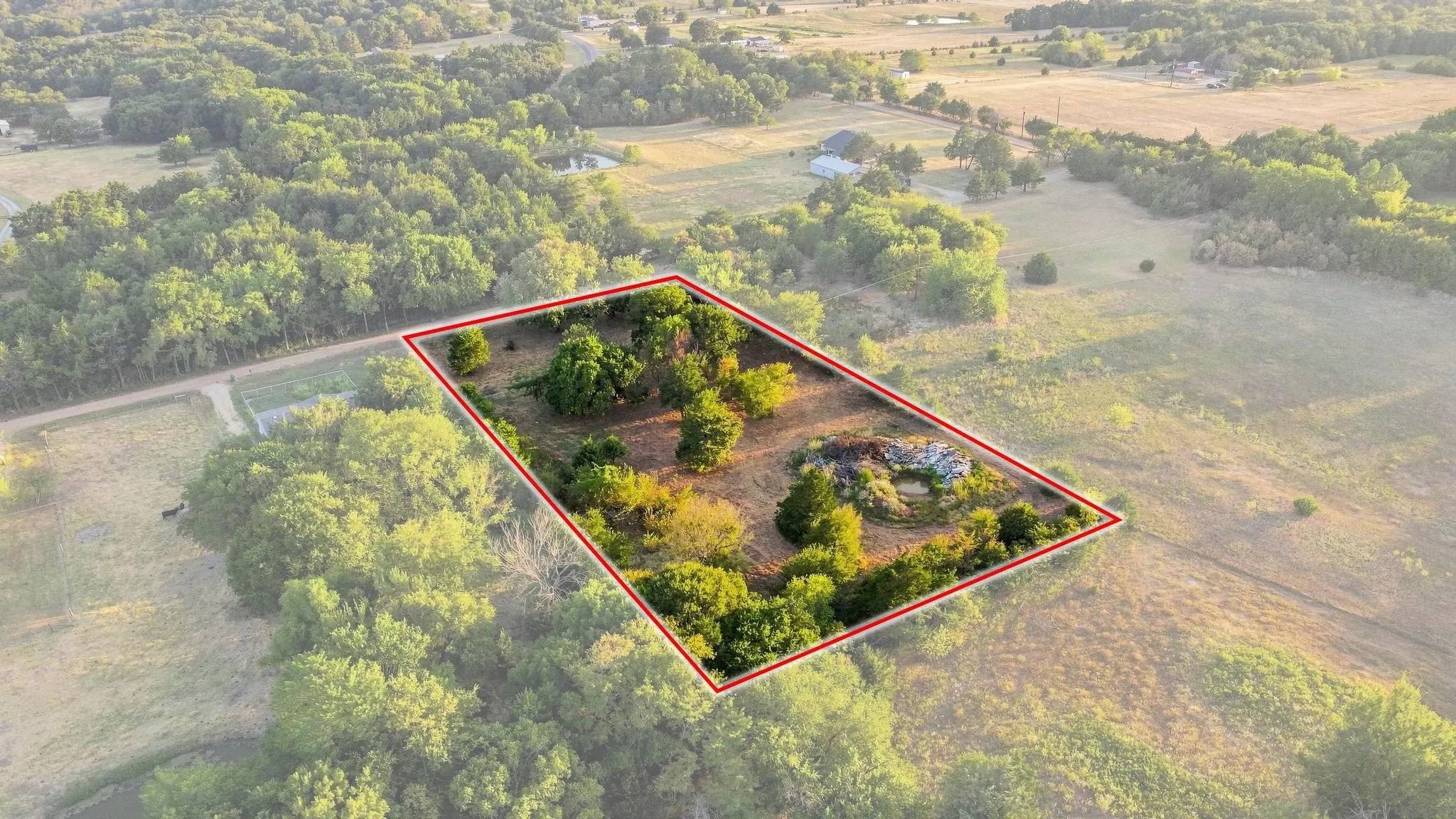 Expansive lot with mature trees and a substantial cleared area, set within a verdant landscape