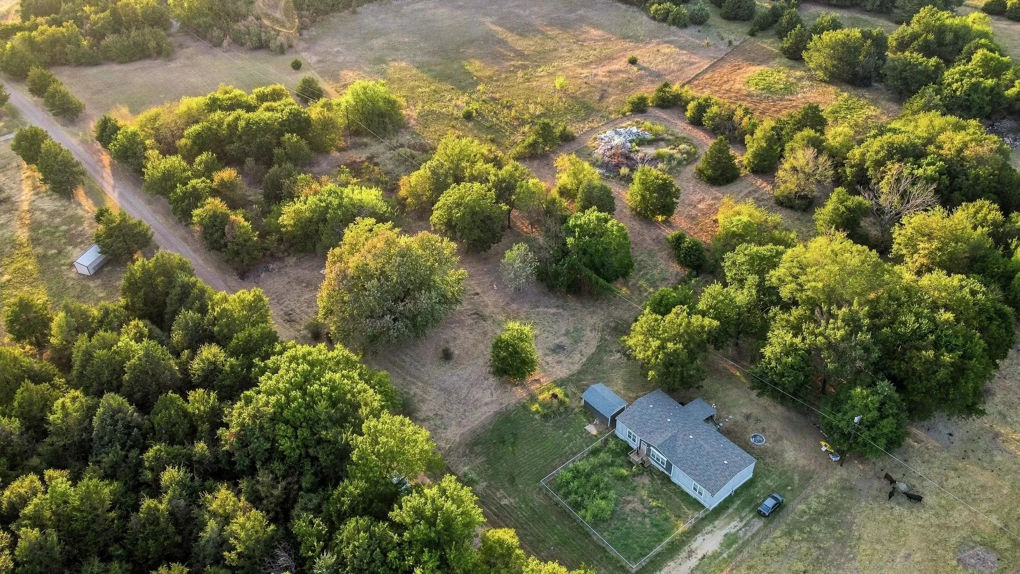 Expansive property featuring a single-story residence, gravel driveway, and mature trees