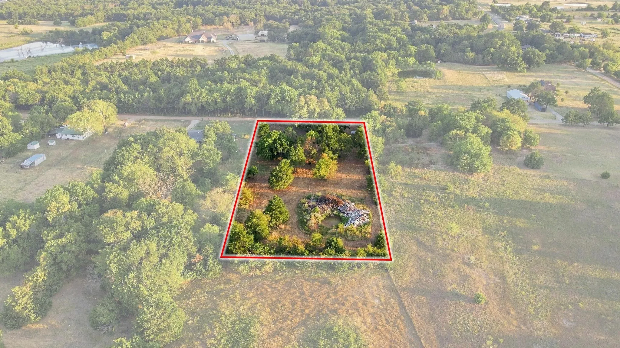 Expansive undeveloped lot with mature trees, surrounded by open land and distant wooded areas