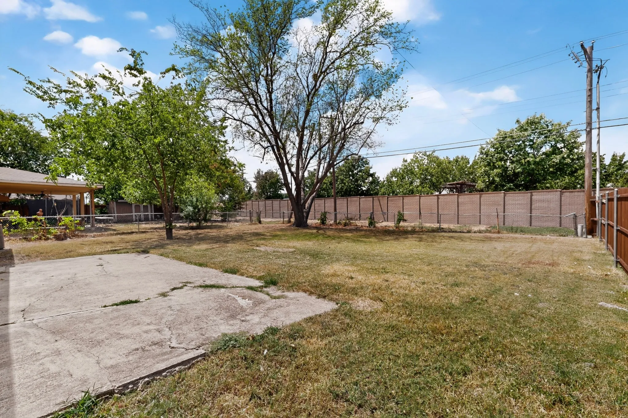 A peaceful backyard scene with a patio featuring a chain link fence and vibrant trees, creating a cozy outdoor space.