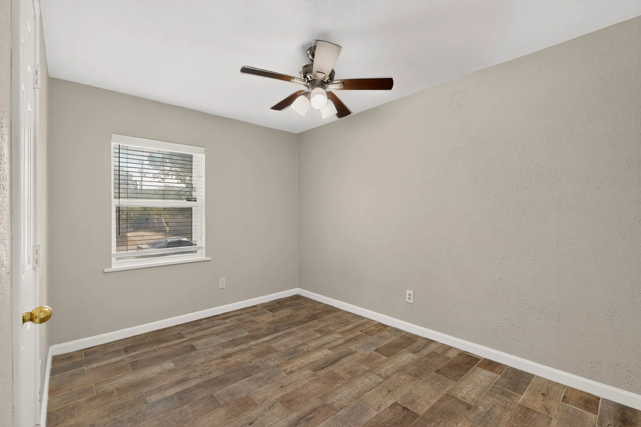 A well-lit third bedroom with a ceiling fan and a window providing a view outside.