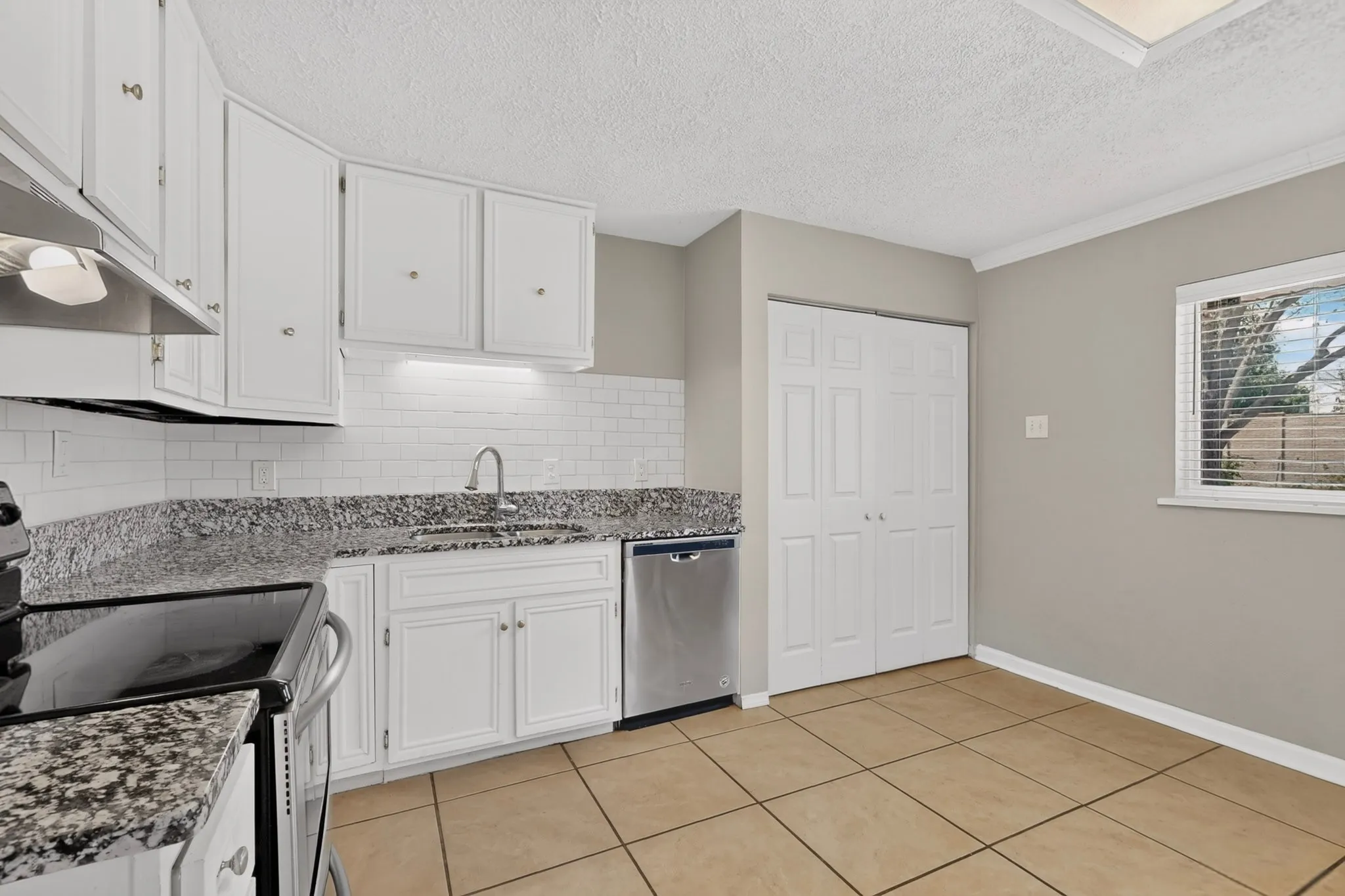 A contemporary kitchen showcasing a wide window, white cabinetry and tile flooring, perfect for meal preparation and family gatherings.

