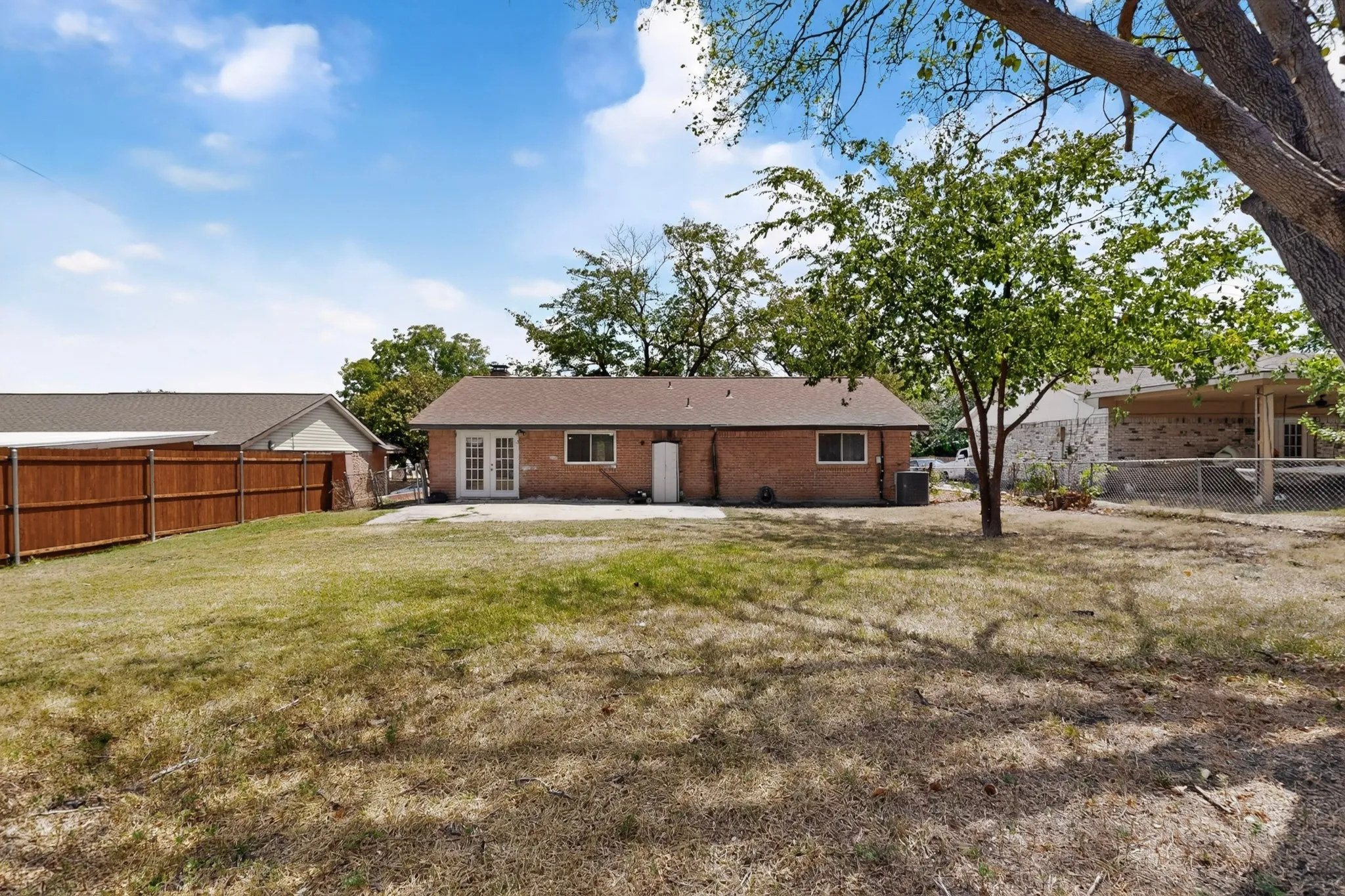 A grassy yard with a patio and a lush tree enclosed by a wooden fence, inviting a sense of tranquility.