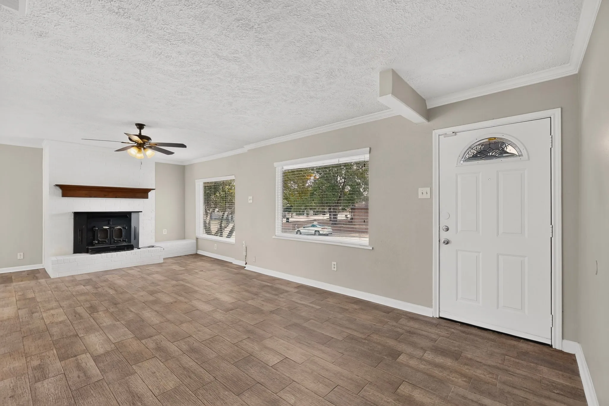 A spacious living room featuring hardwood floors, a fireplace, a ceiling fan and wide windows, perfect for relaxation and gatherings.