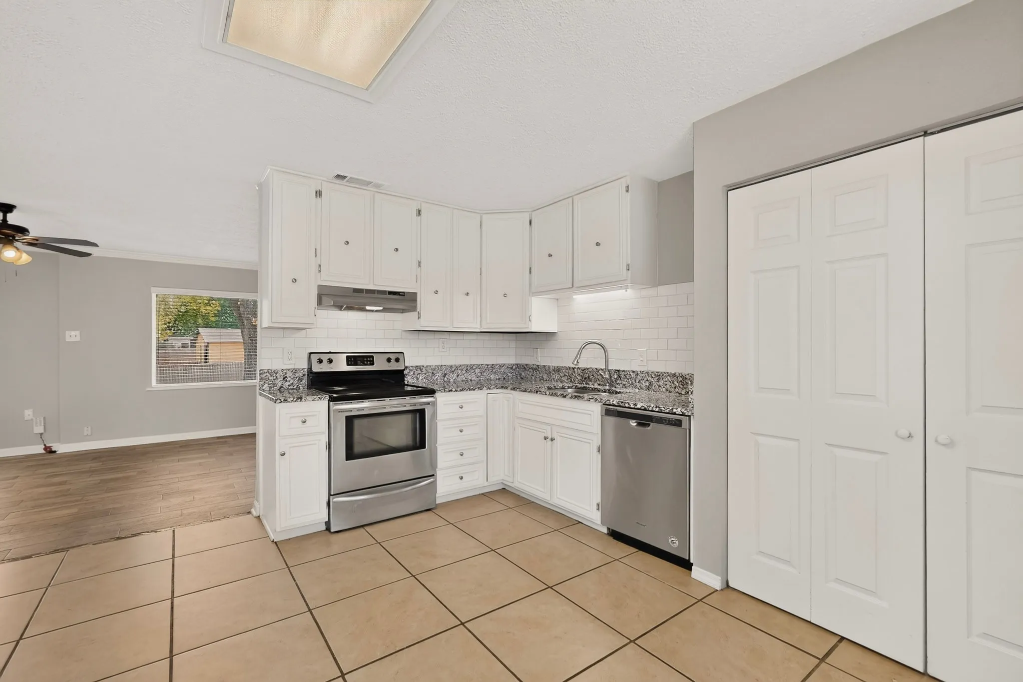 Bright kitchen with sleek white cabinets, stainless steel appliances and tile flooring, designed for functionality and style.