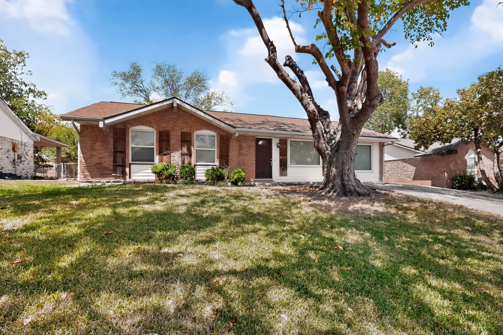 A charming brick home set in a large yard, featuring a green yard and a large tree for shade and beauty.