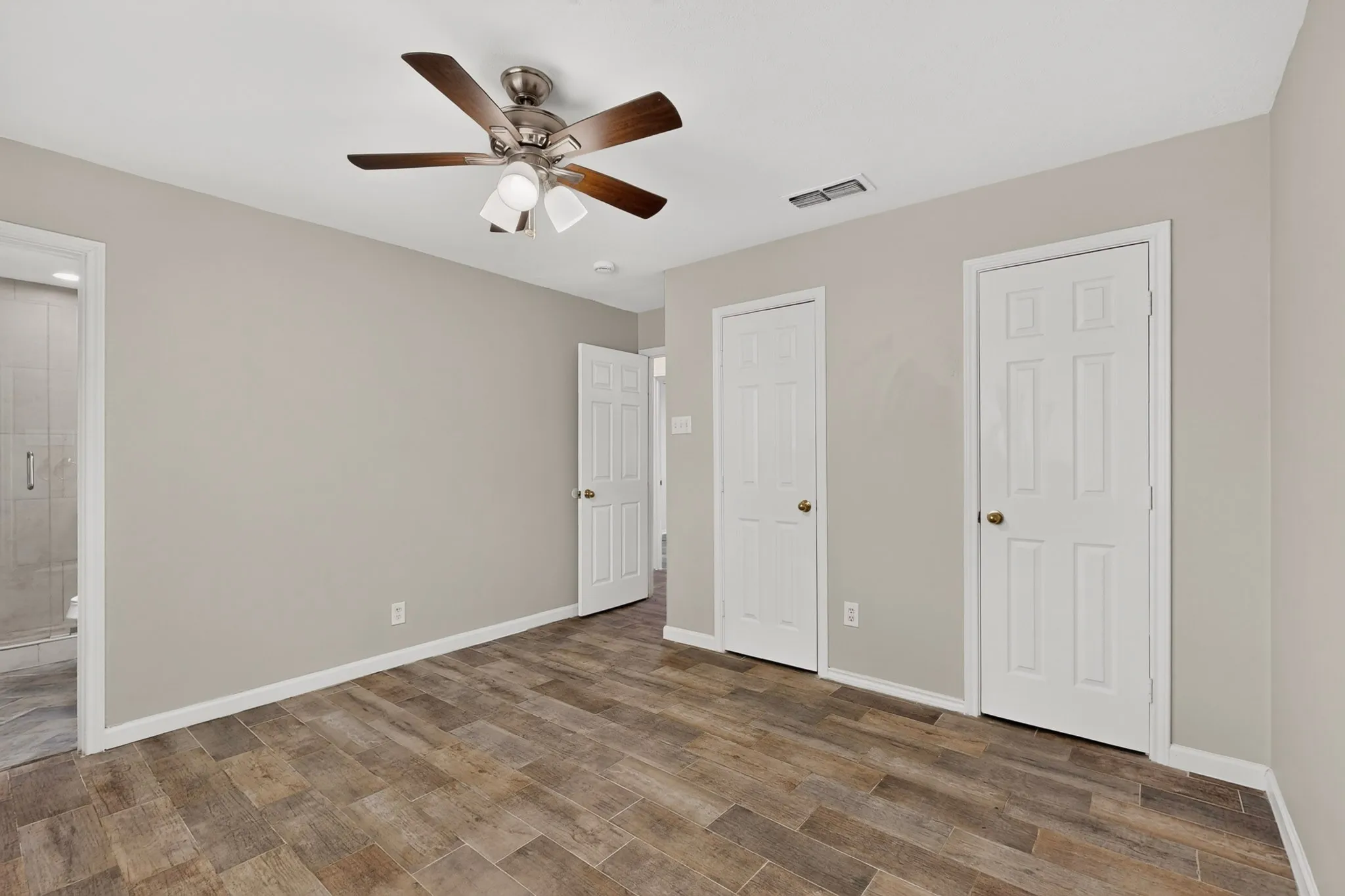 Bright primary bedroom with a ceiling fan, hardwood floors, two separate closets and an en suite bath, perfect for relaxation.