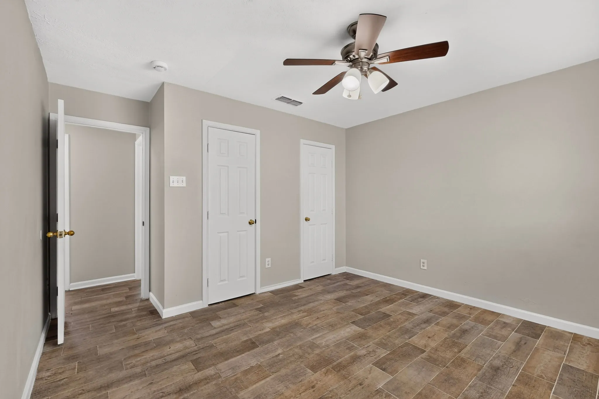 Bright primary bedroom with a ceiling fan, hardwood floors and two separate closets, perfect for relaxation.
