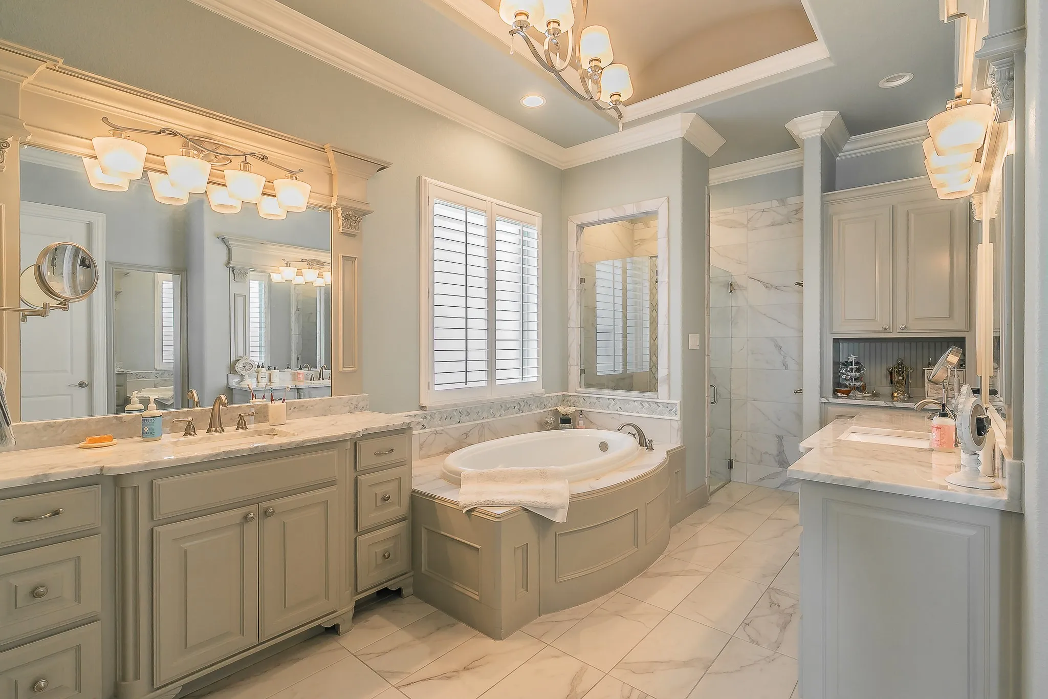 Spa-inspired primary bathroom featuring dual vanities with marble-finish countertops, an oversized soaking tub with built-in surround, a walk-in shower with glass enclosure, coffered ceiling detail, and recessed lighting throughout