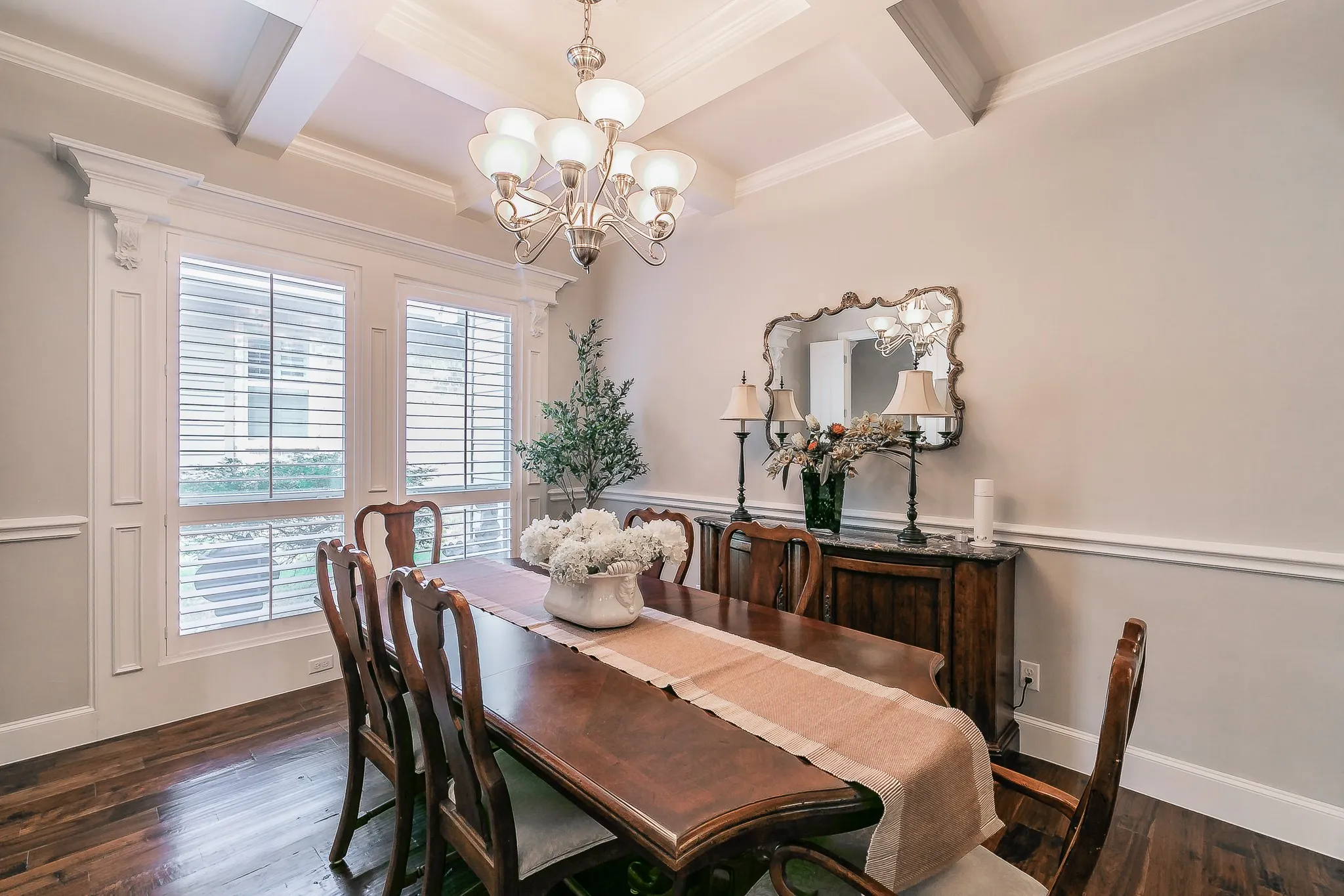 Coffered ceiling featuring a chandelier, wood flooring, white plantation shutters, decorative wall molding, and crown molding