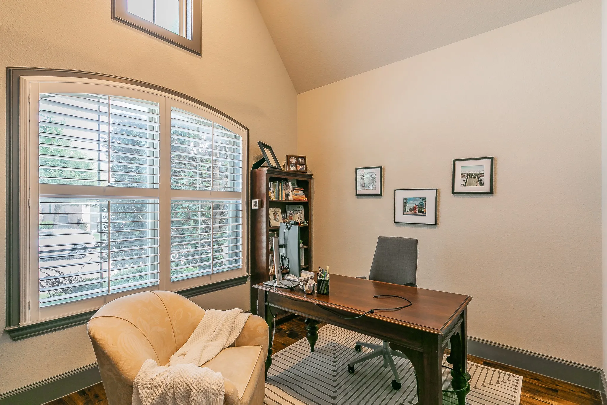 Wood-finish flooring, vaulted ceiling, arched window with plantation shutters, and a built-in wood bookshelf