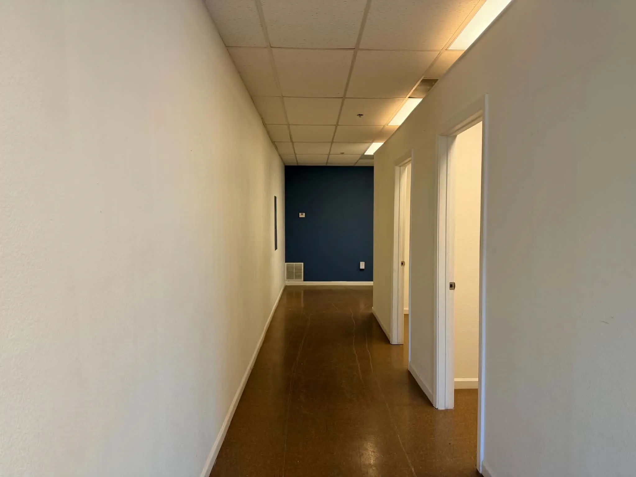 Hallway featuring durable flooring, drop ceiling with integrated lighting, and multiple entryways