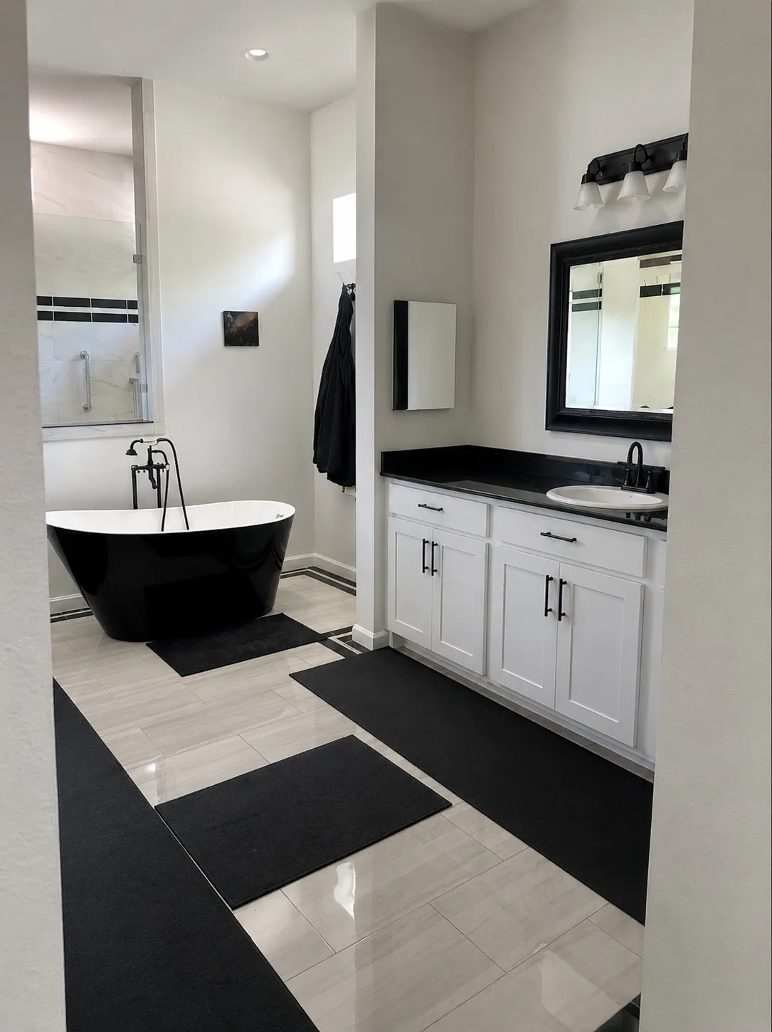 Freestanding black soaking tub, dual-sink vanity with white cabinetry, dark countertops, and a framed mirror, and light-toned tile flooring with dark accents