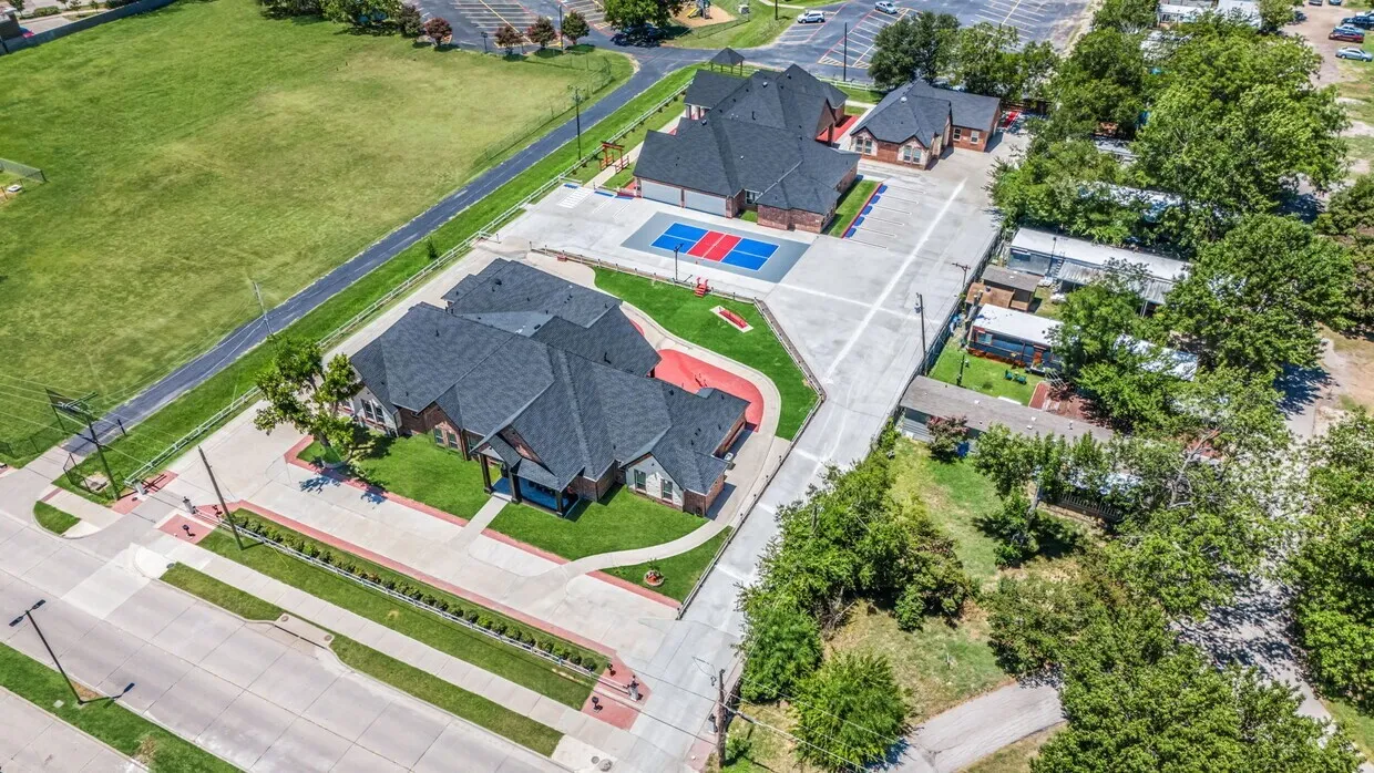 Two substantial buildings with dark shingle roofs, expansive concrete paving, and a dedicated sports court
