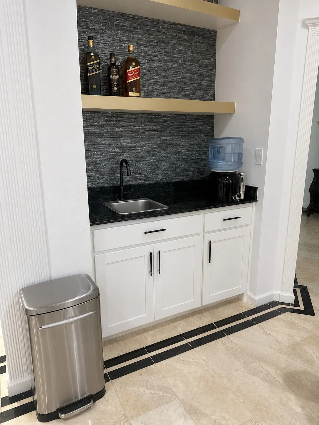 Built-in wet bar with white cabinetry, dark countertop, and stone-finish backsplash
