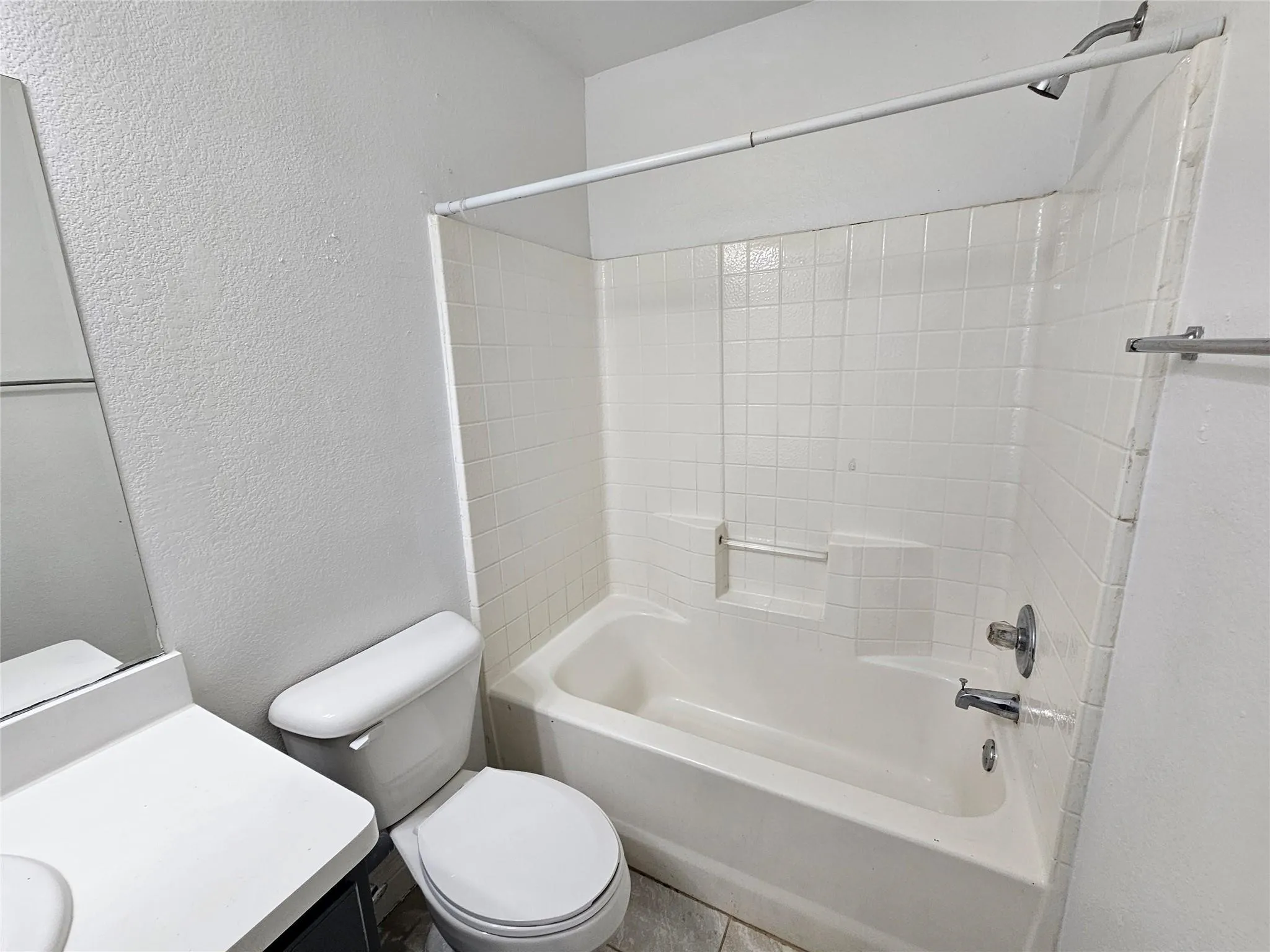 White tiled shower/tub combination with a built-in shelf, adjacent toilet, and vanity with a countertop