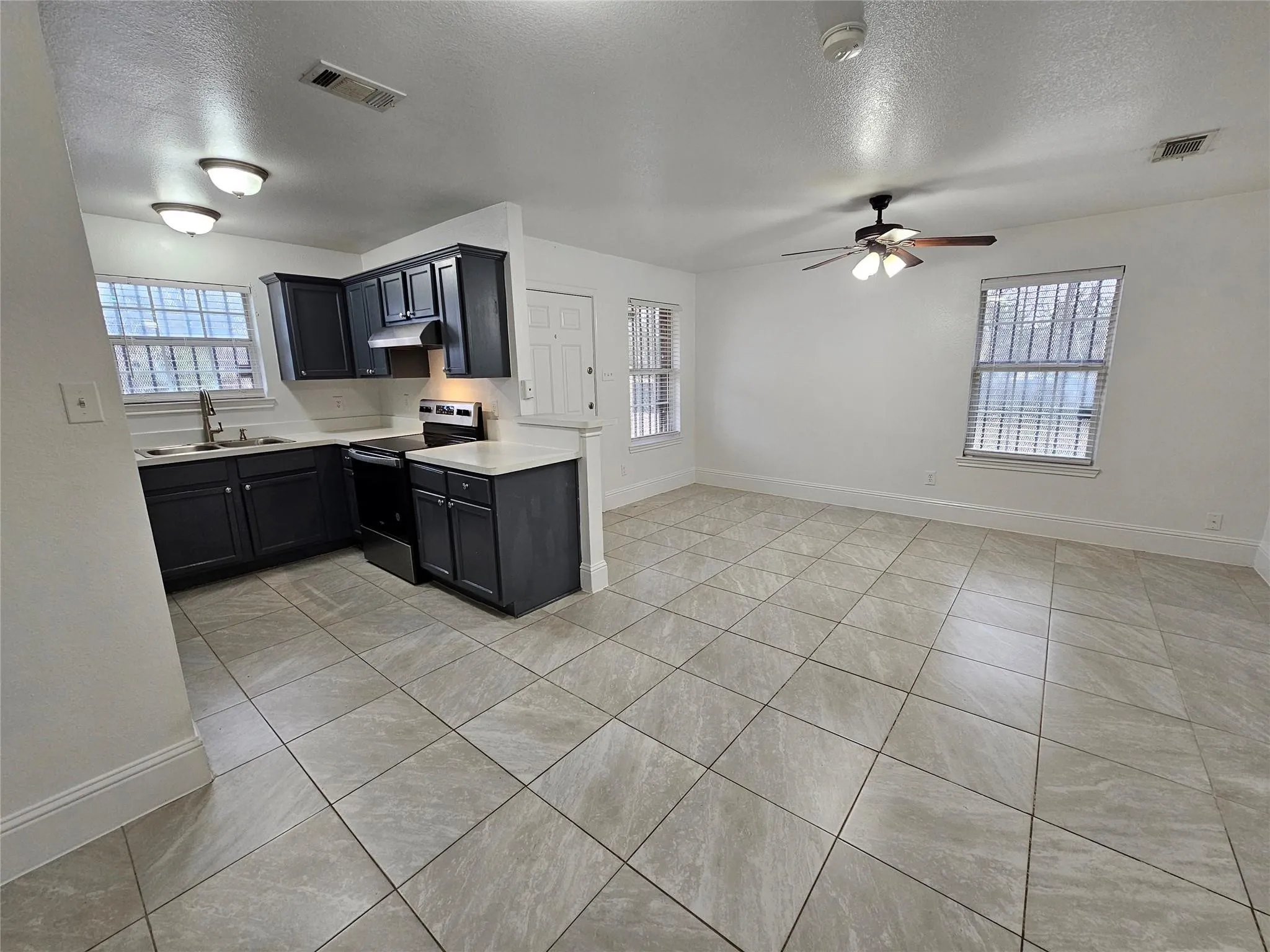 Open-concept living space with tile flooring, dark cabinetry, light countertops, and a ceiling fan