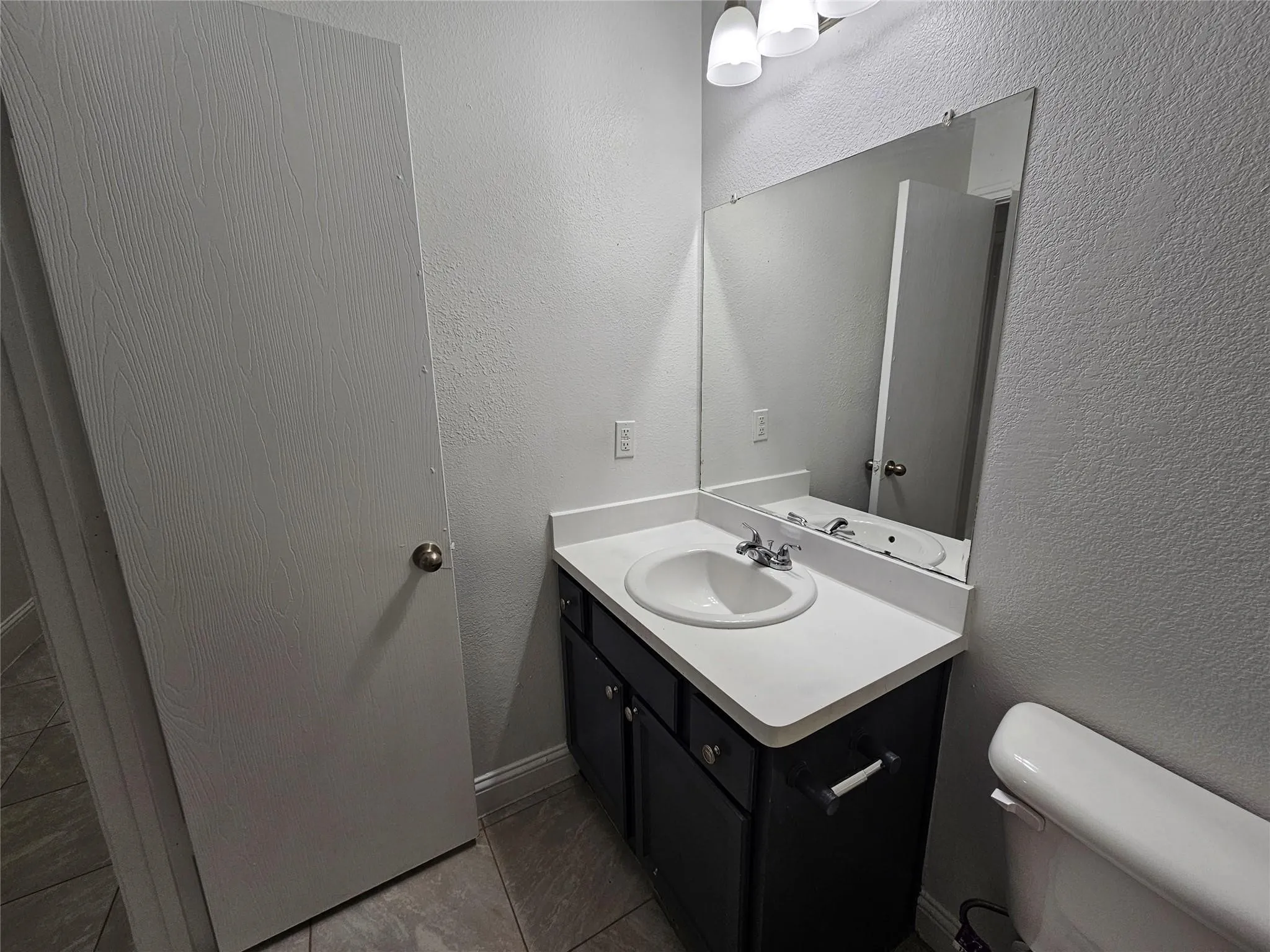 Vanity with a white countertop and integrated sink, chrome faucet, wall-mounted mirror, and tile flooring