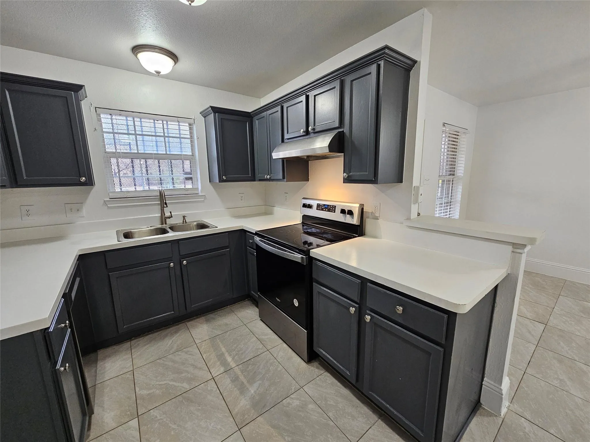 Modern kitchen featuring dark cabinetry, stainless steel sink, contemporary faucet, stainless steel electric range, and tile flooring