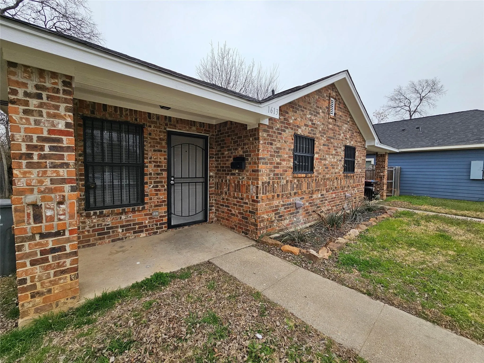 Brick exterior with a covered porch, front entry door with security screen, and a concrete walkway