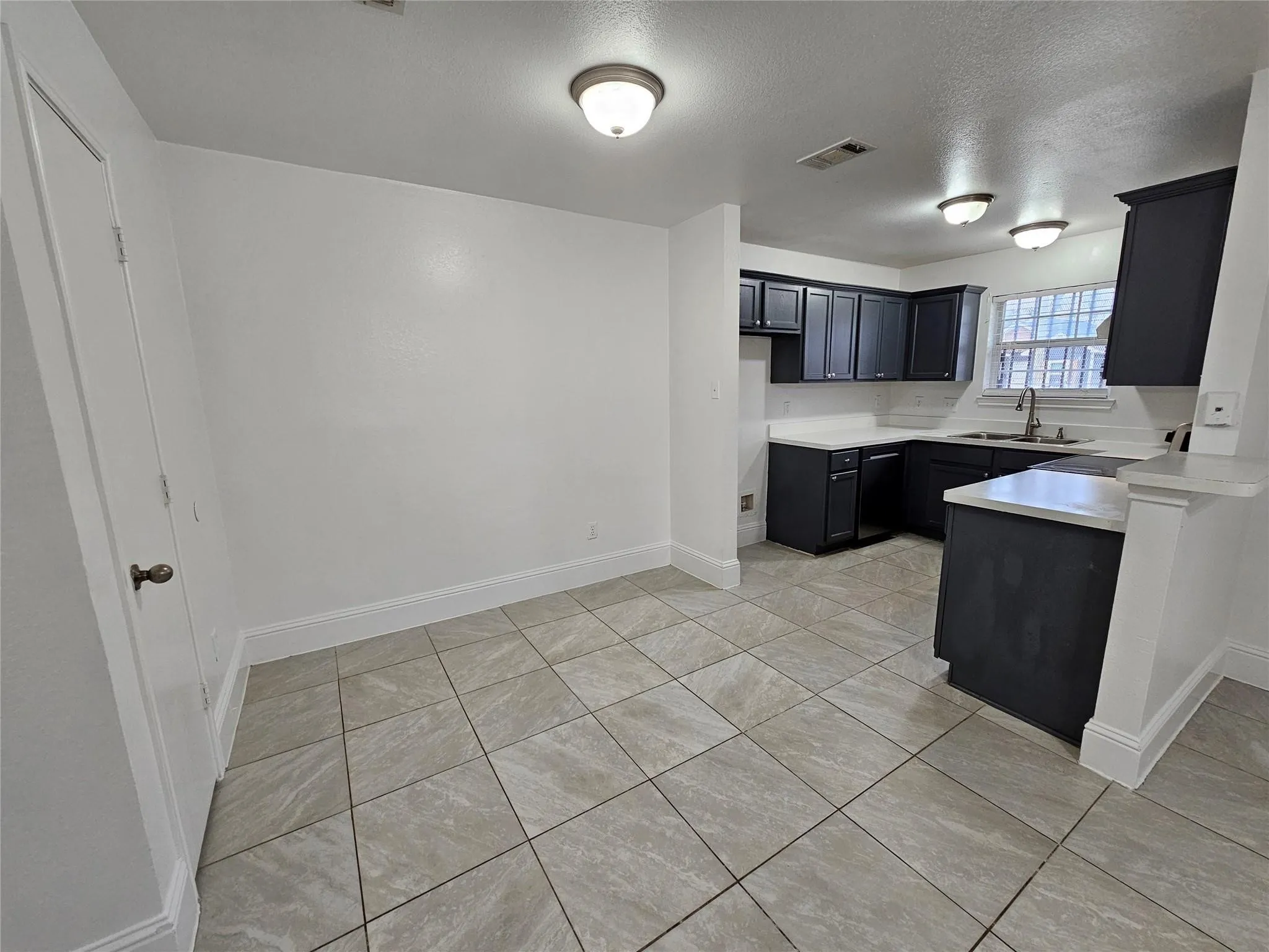 Kitchen and dining area featuring tile flooring, dark cabinetry, light countertops, and a stainless steel sink