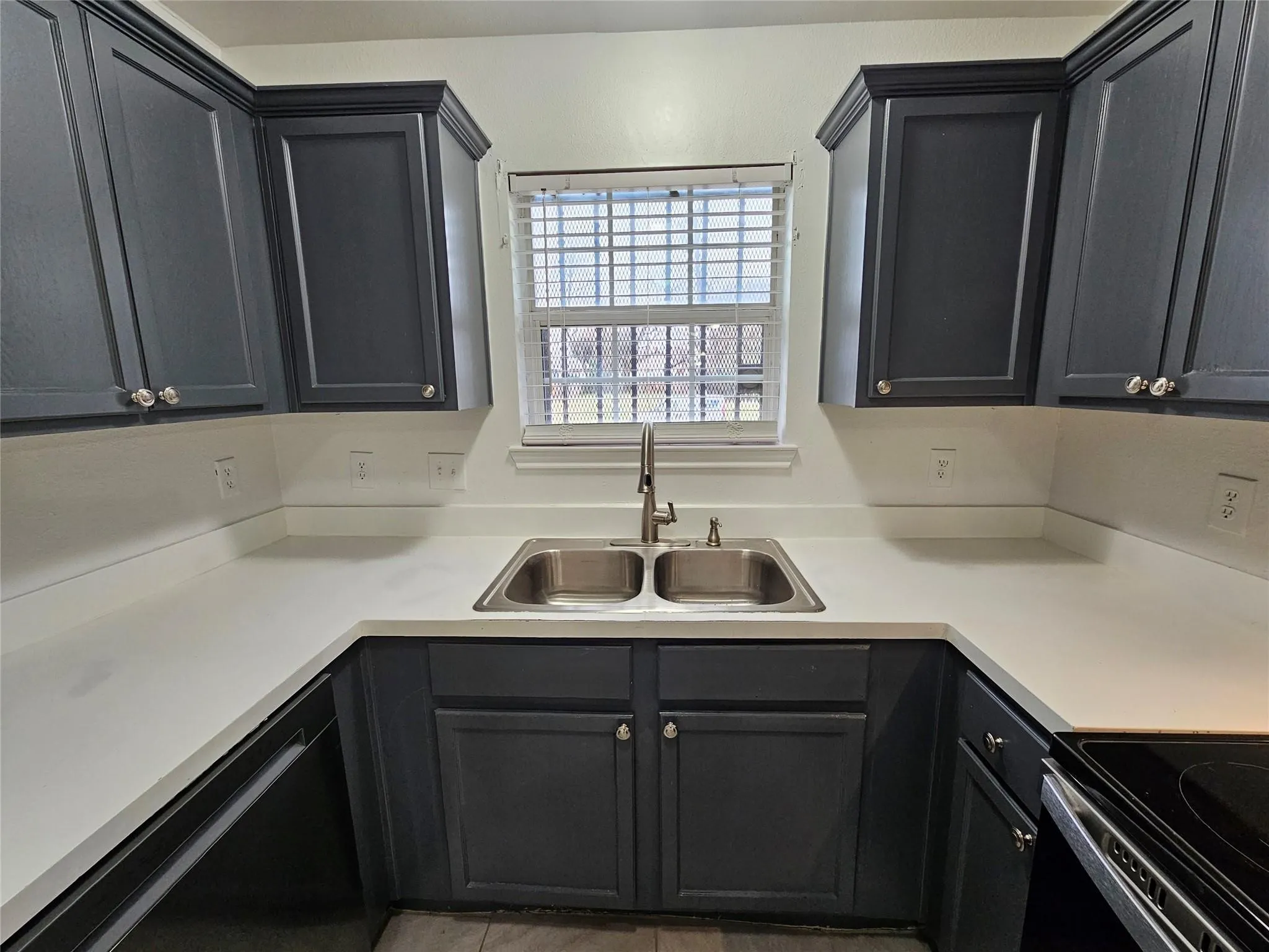 U-shaped countertop with a dual basin stainless steel sink, framed by dark cabinetry and a window with blinds