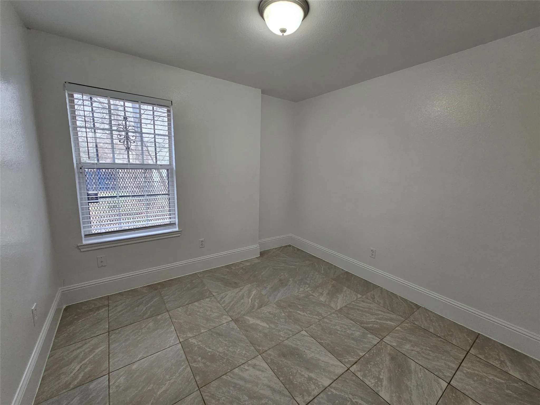 Neutral wall color with textured finish, tiled flooring, window with horizontal blinds, and a ceiling-mounted light fixture