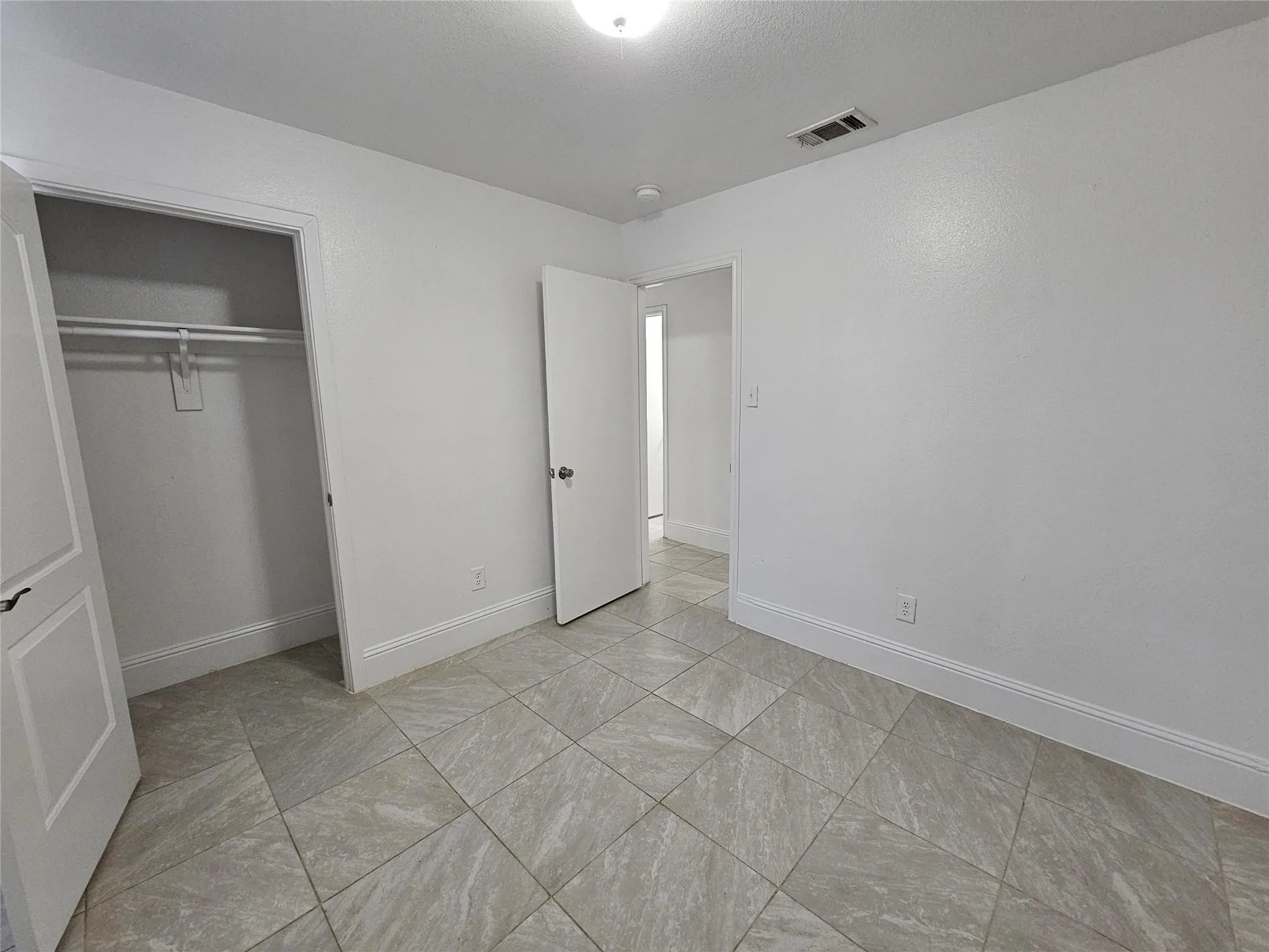 Square tile flooring, white walls, recessed ceiling light, and a built-in closet with hanging rod