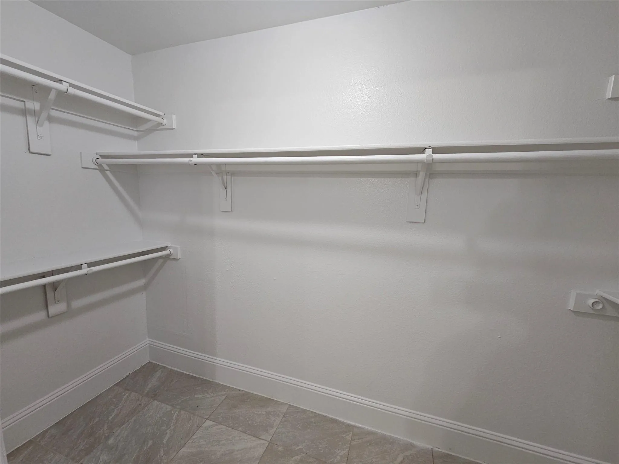 Walk-in closet with multiple white shelving units and hanging rods, complemented by light-toned tile flooring and white trim
