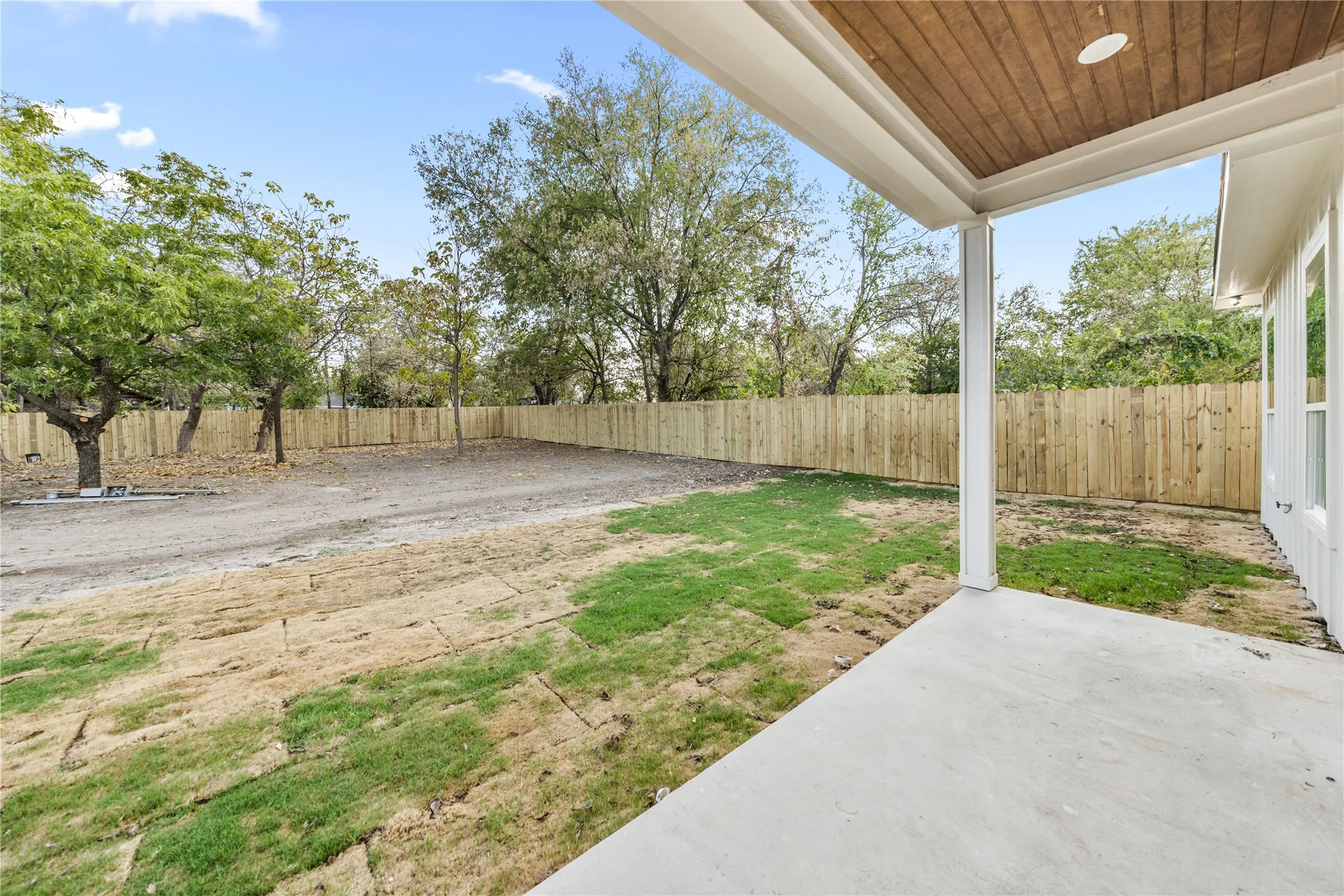 Covered concrete patio with wood-finish ceiling, white columns, and a newly installed wood privacy fence