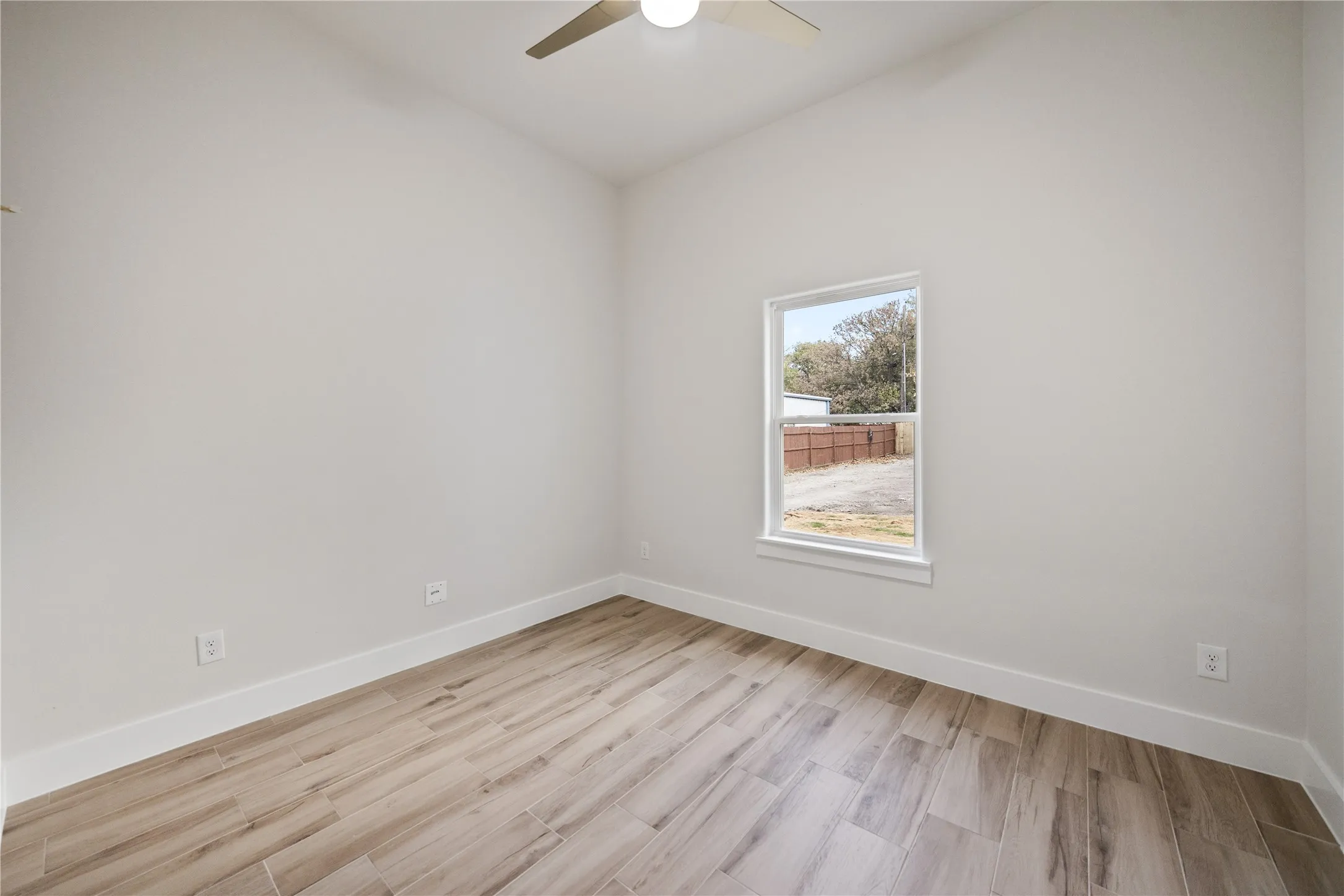 Vaulted ceiling with a ceiling fan, window with white trim, and wood-finish flooring