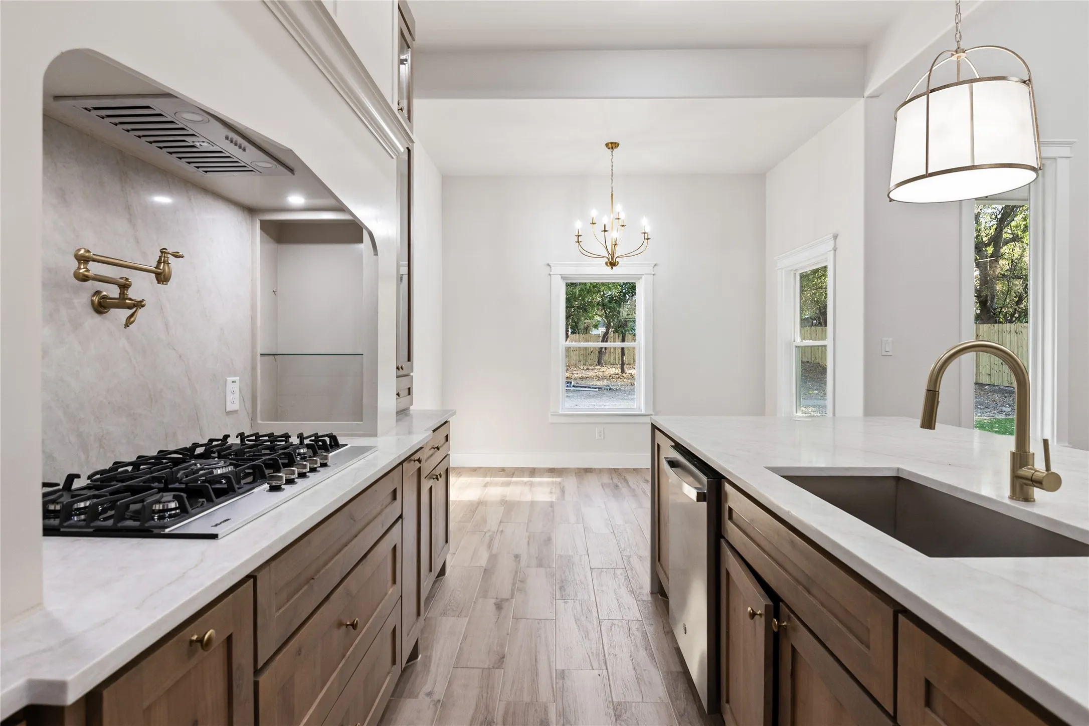 Gourmet kitchen with a gas range, pot filler, wood-finish cabinetry, white countertops, and a modern island pendant light
