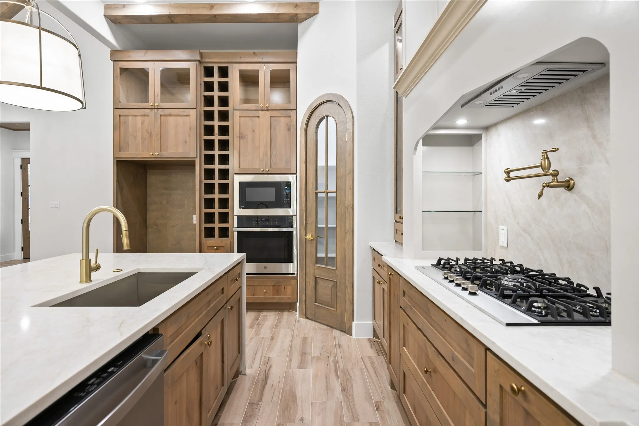 Kitchen featuring an island with an undermount sink, built-in stainless steel appliances, wood-finish flooring, and natural wood cabinetry