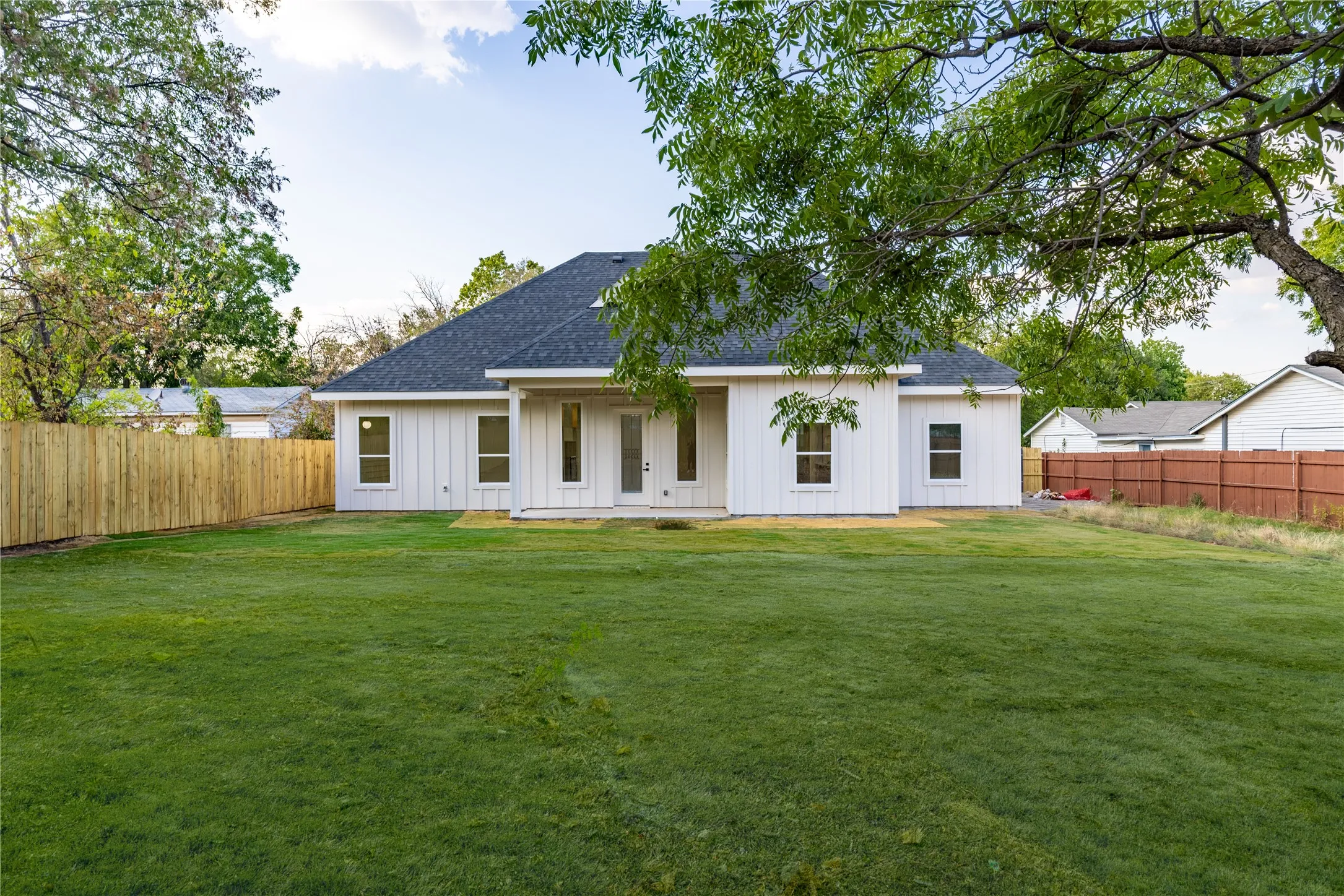 Expansive backyard featuring a manicured lawn, a newly installed wood fence, and a white exterior home with a dark shingle roof