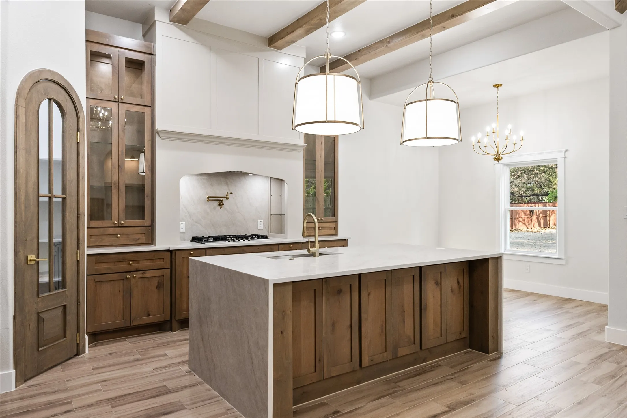 Kitchen featuring wood-finish flooring, exposed wood ceiling beams, a central island with a waterfall countertop, custom wood cabinetry, and a gas range
