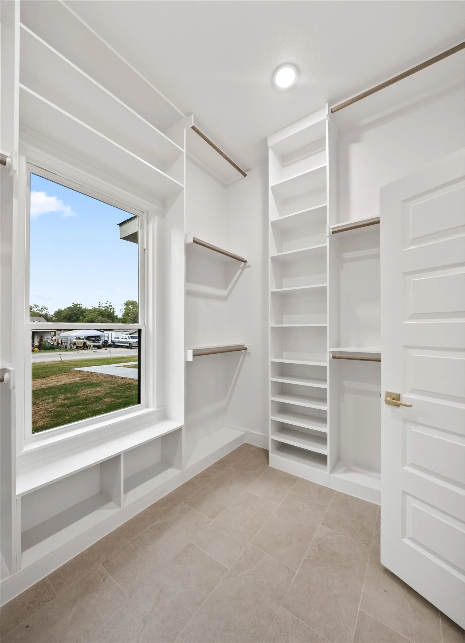 Built-in custom shelving, ample hanging rods, window with integrated bench seating, recessed lighting, and tile flooring