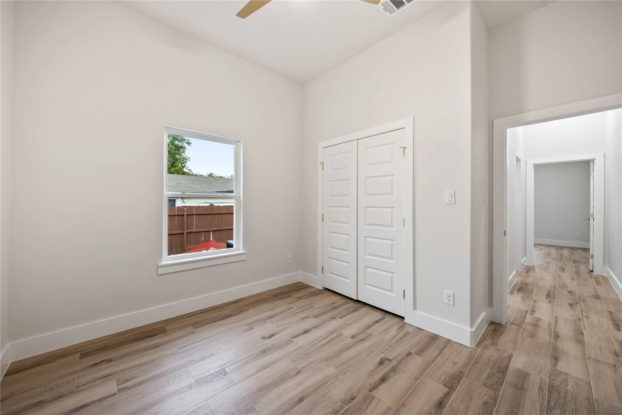 Vaulted ceiling, wood-finish flooring, white trim, window, and bi-fold closet doors