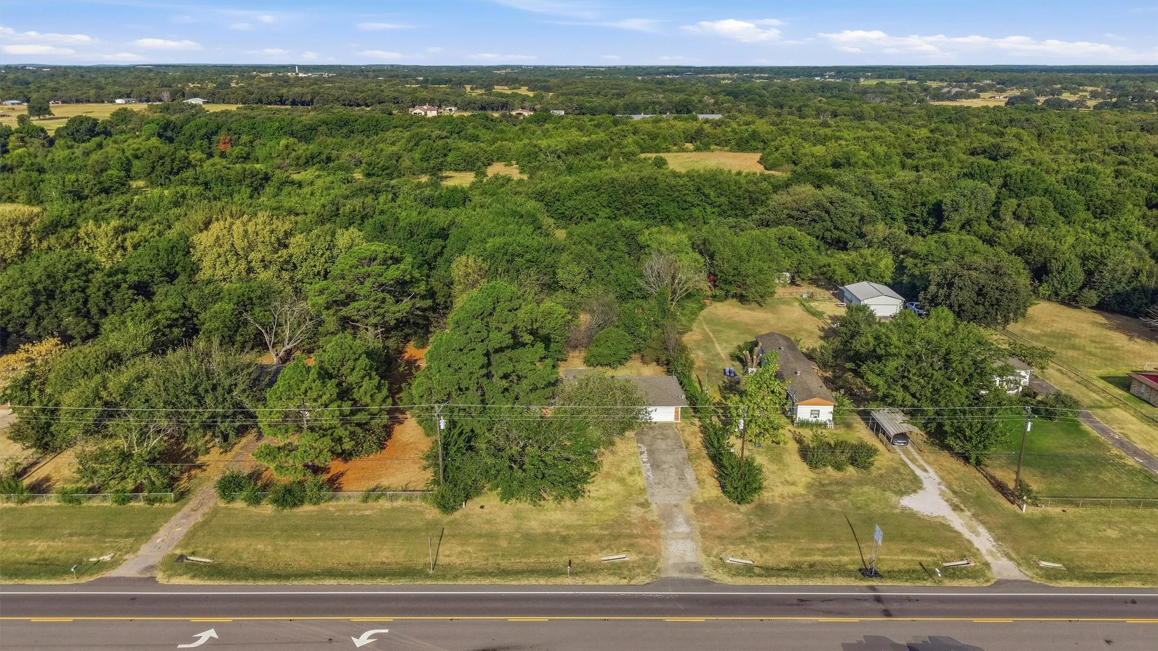 Expansive rural property featuring mature tree coverage, multiple outbuildings, and direct highway frontage